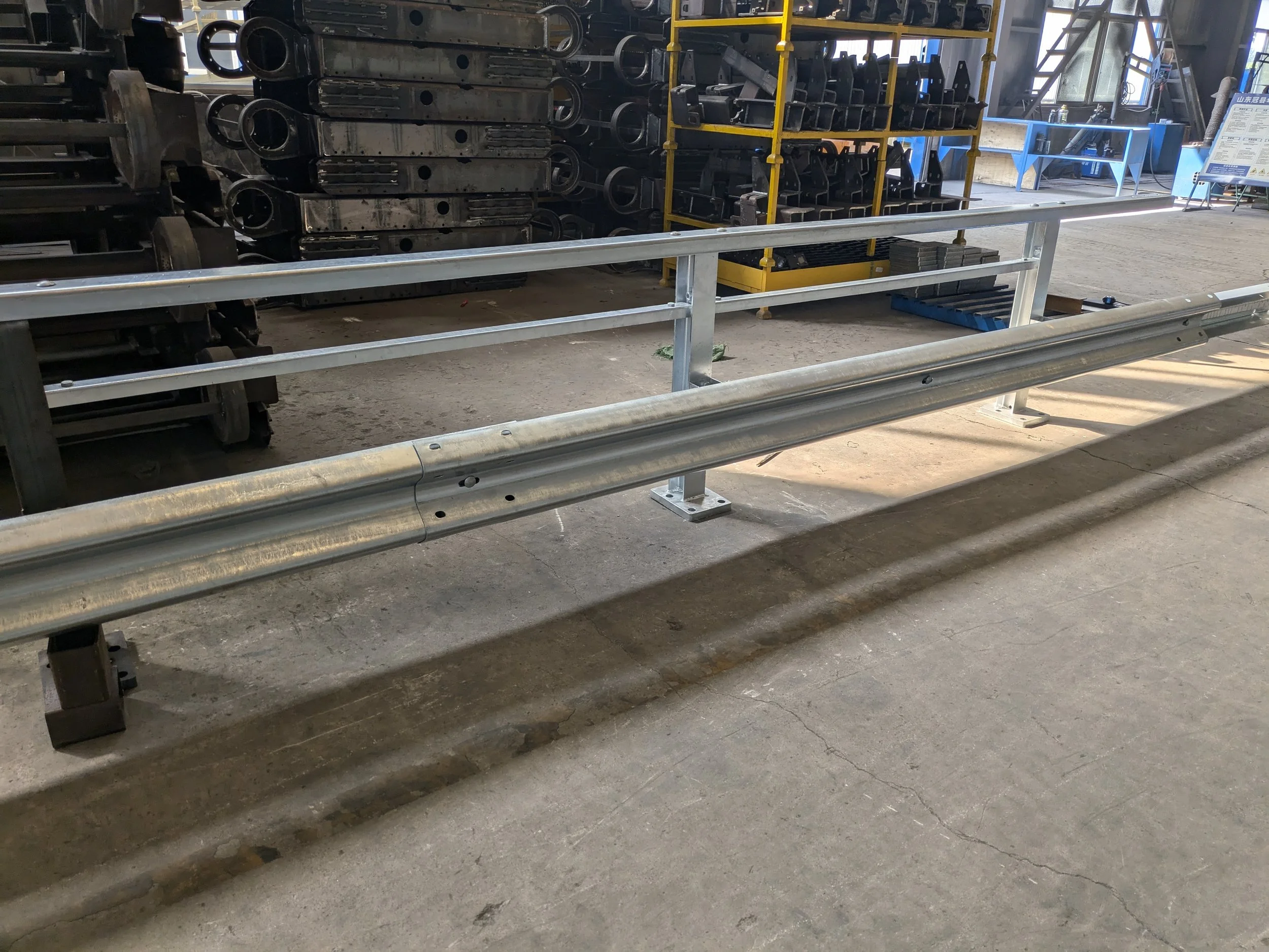 Industrial safety barrier and metal guardrail inside a factory or warehouse with machinery and shelving in the background.