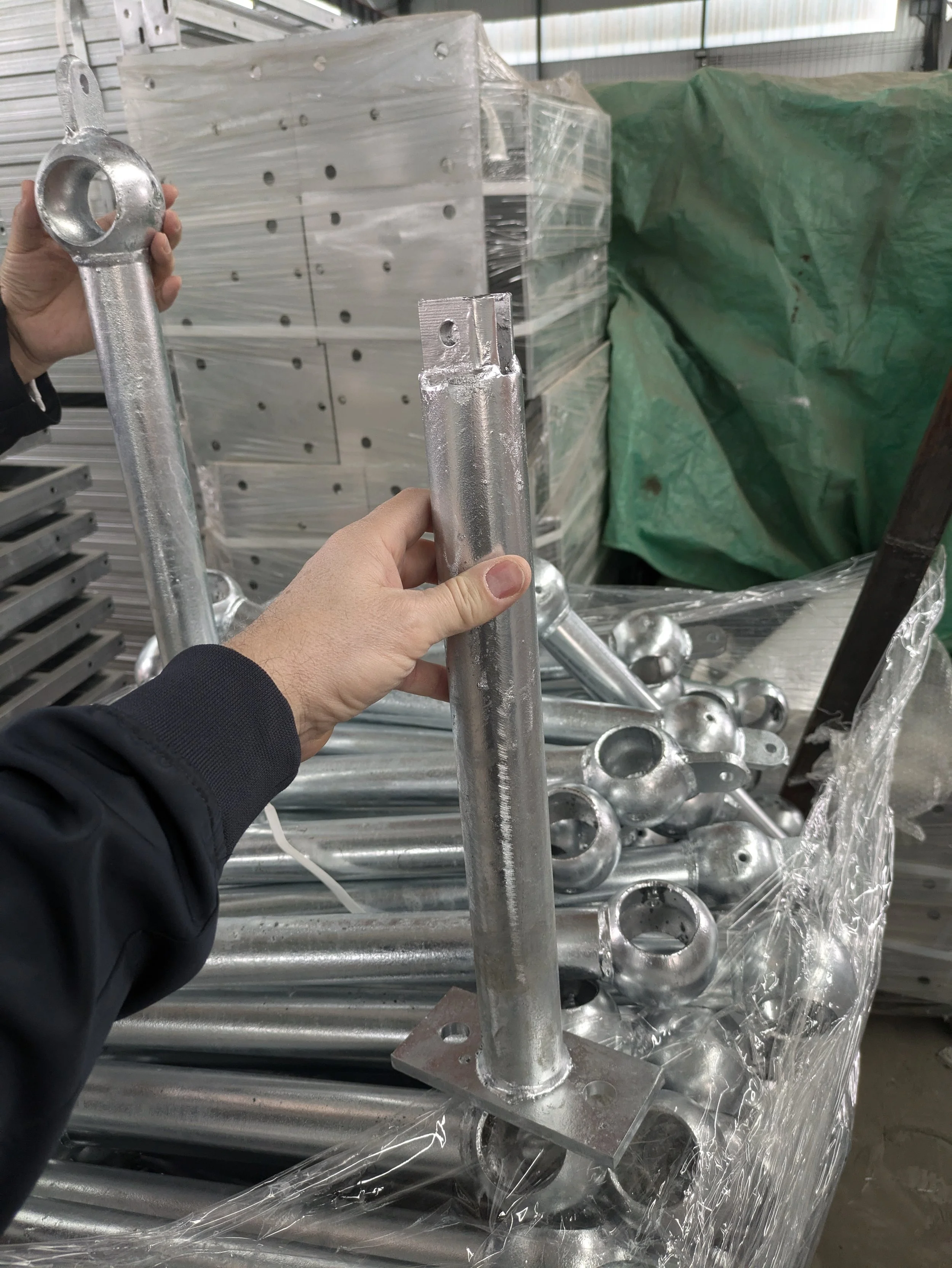 Several metallic pole supports with flat mounting plates being handled at a warehouse or manufacturing facility.