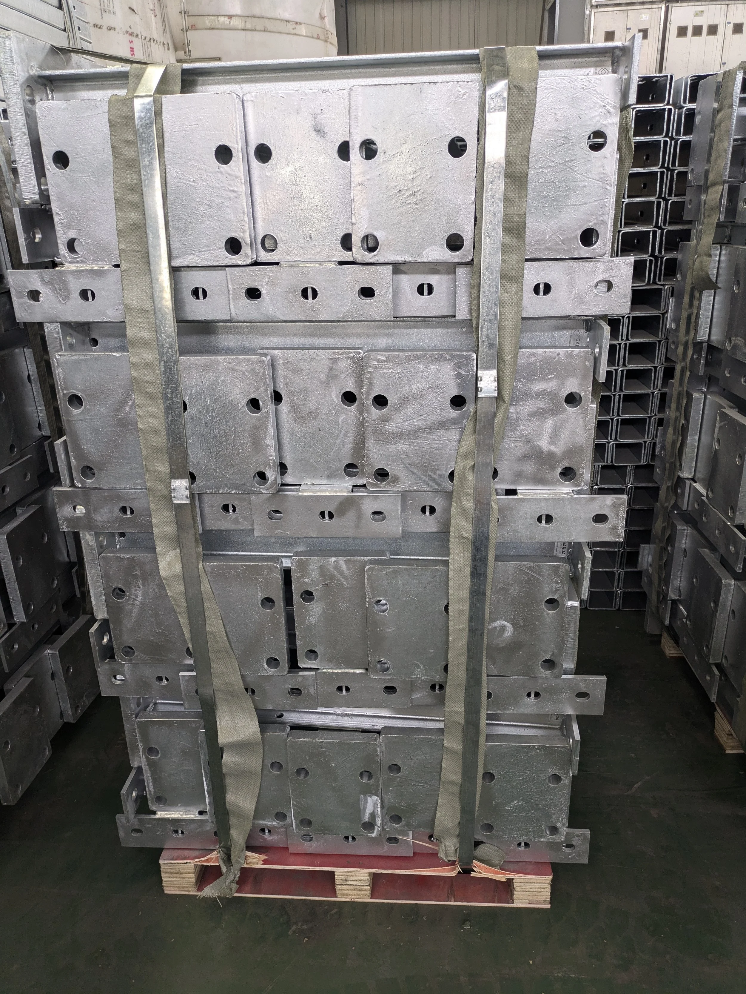 Stack of large metal plates with circular holes, secured with straps on a wooden pallet in an industrial warehouse.