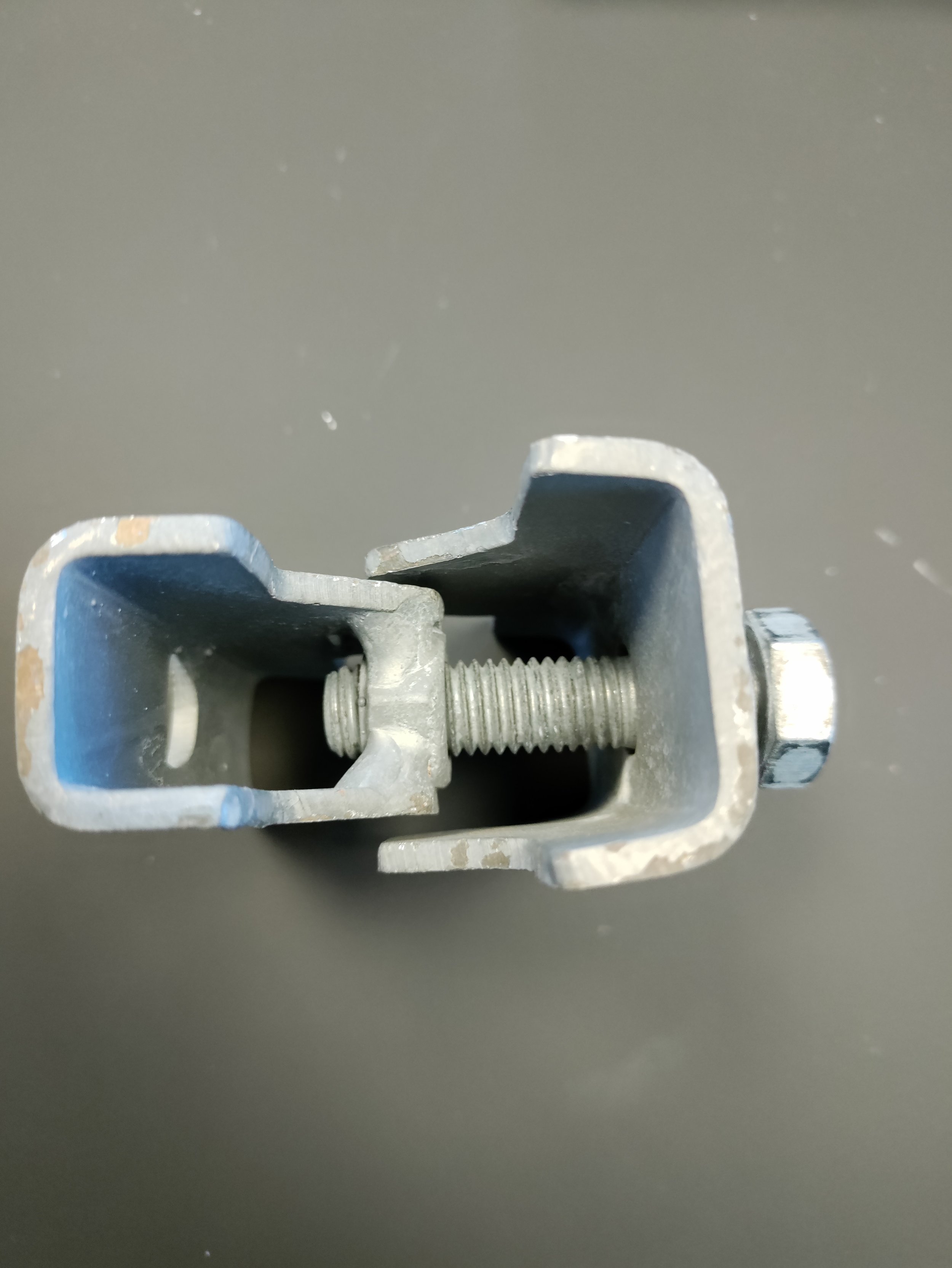 A metal clamp with a screw mechanism, seen from above, on a gray surface.