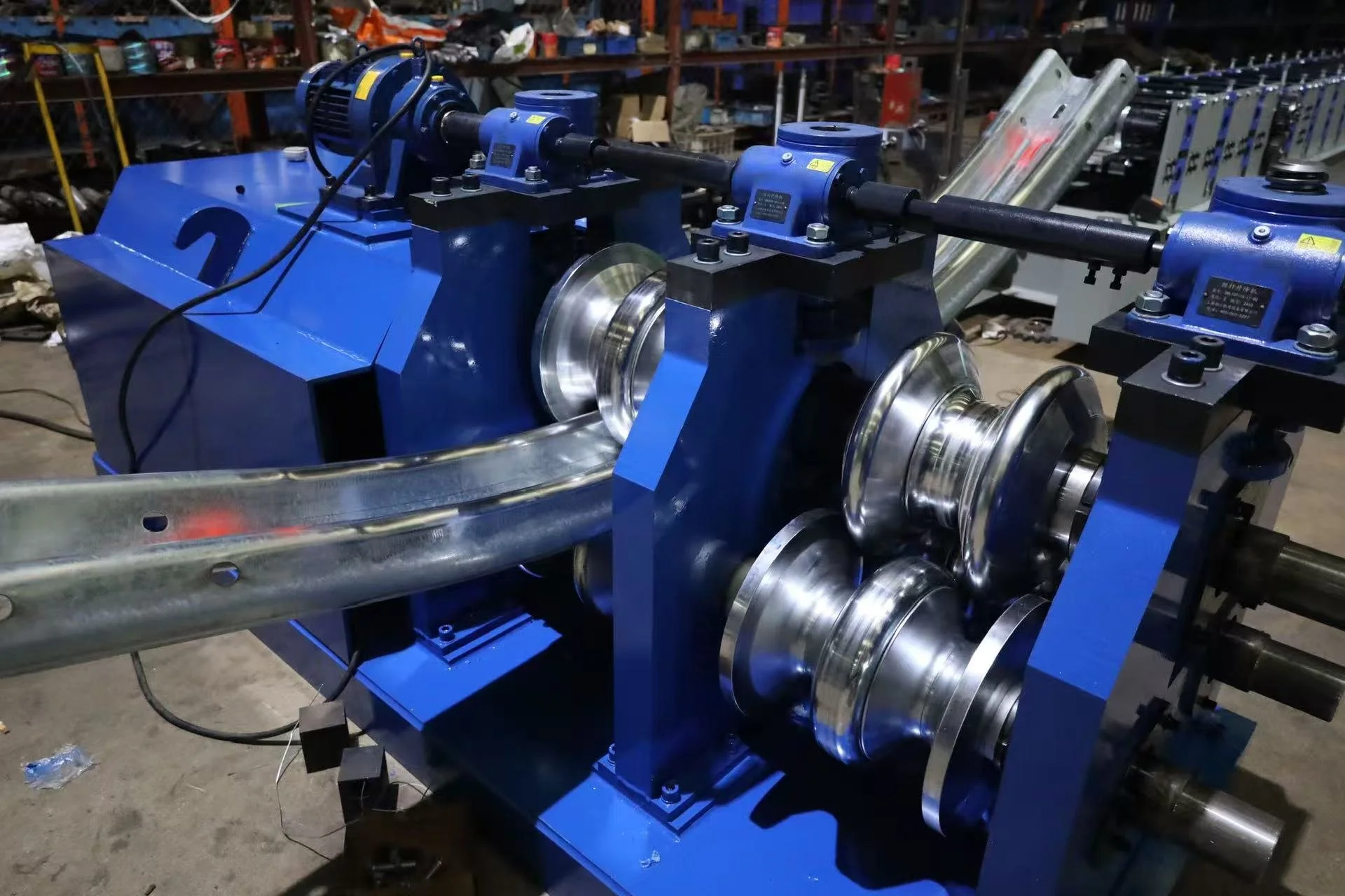 Industrial machine with blue components and metal rollers in a workshop or factory environment.