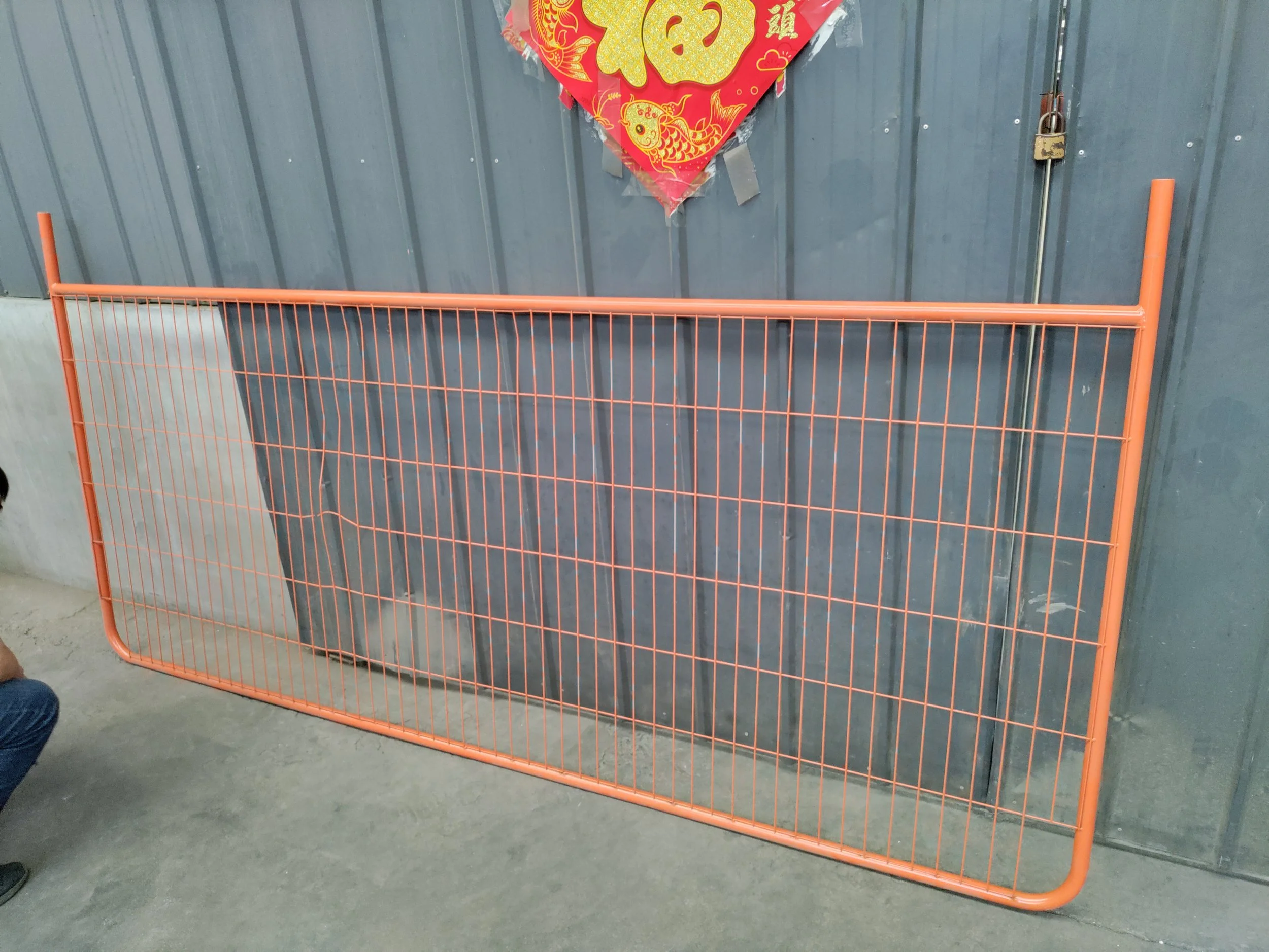 Orange metal crowd control barrier in front of a gray metal wall with a red and gold Chinese New Year decoration hanging above.