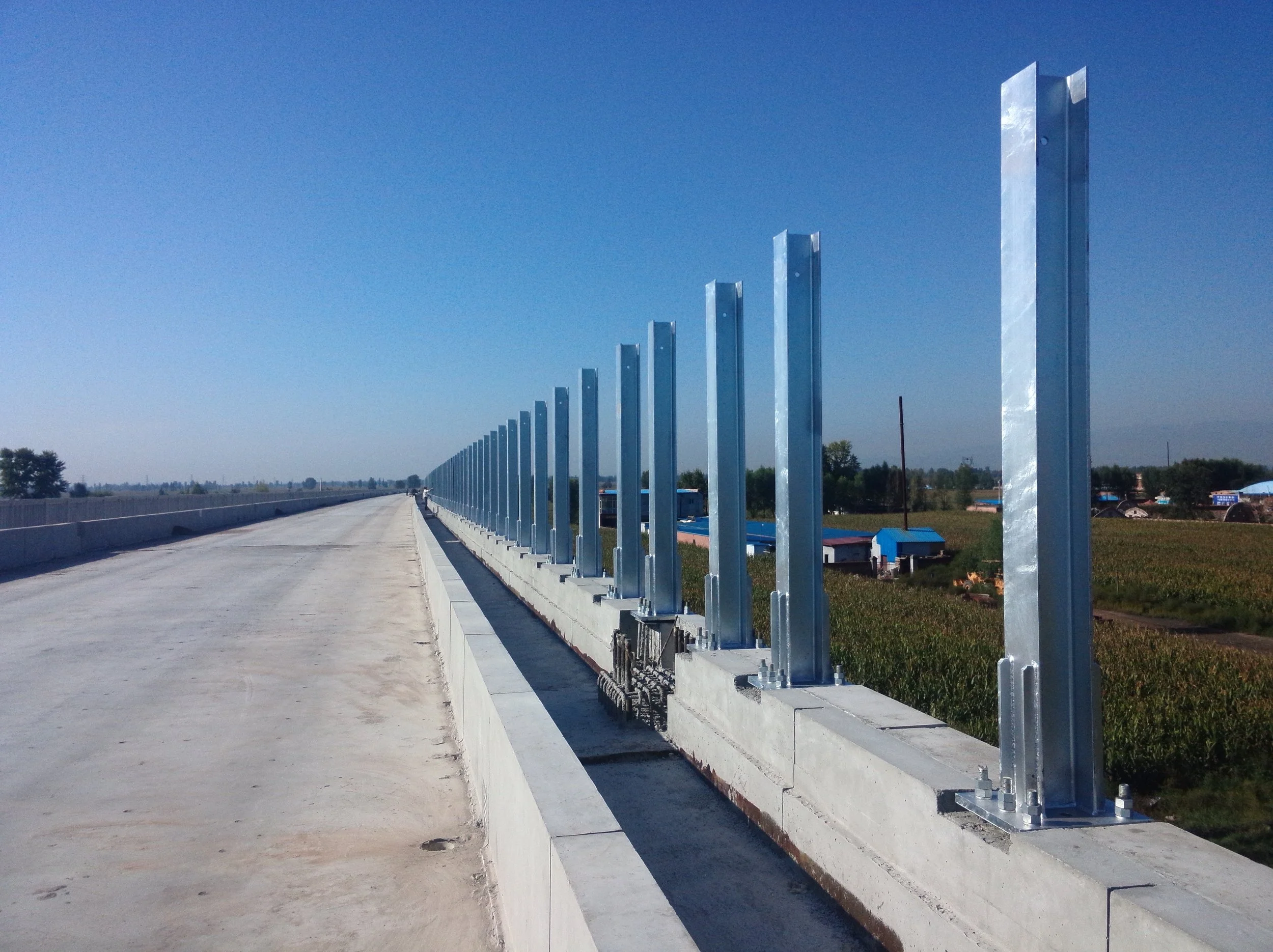 Newly constructed bridge with metal railings and concrete barriers, extending into the distance with a clear blue sky and rural landscape in the background.