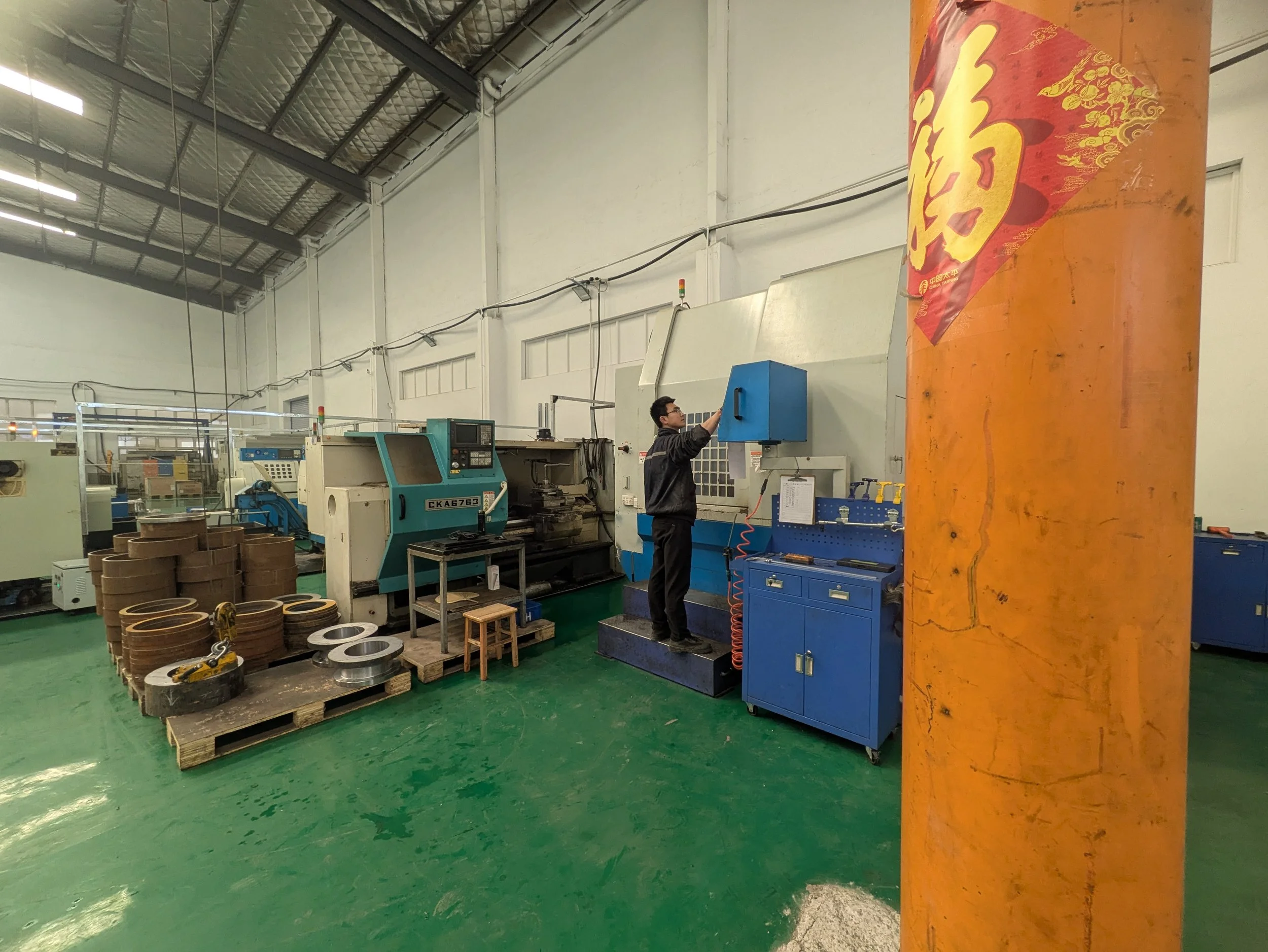 A man working with machinery in an industrial factory setting, with various machines, components, and tools around.