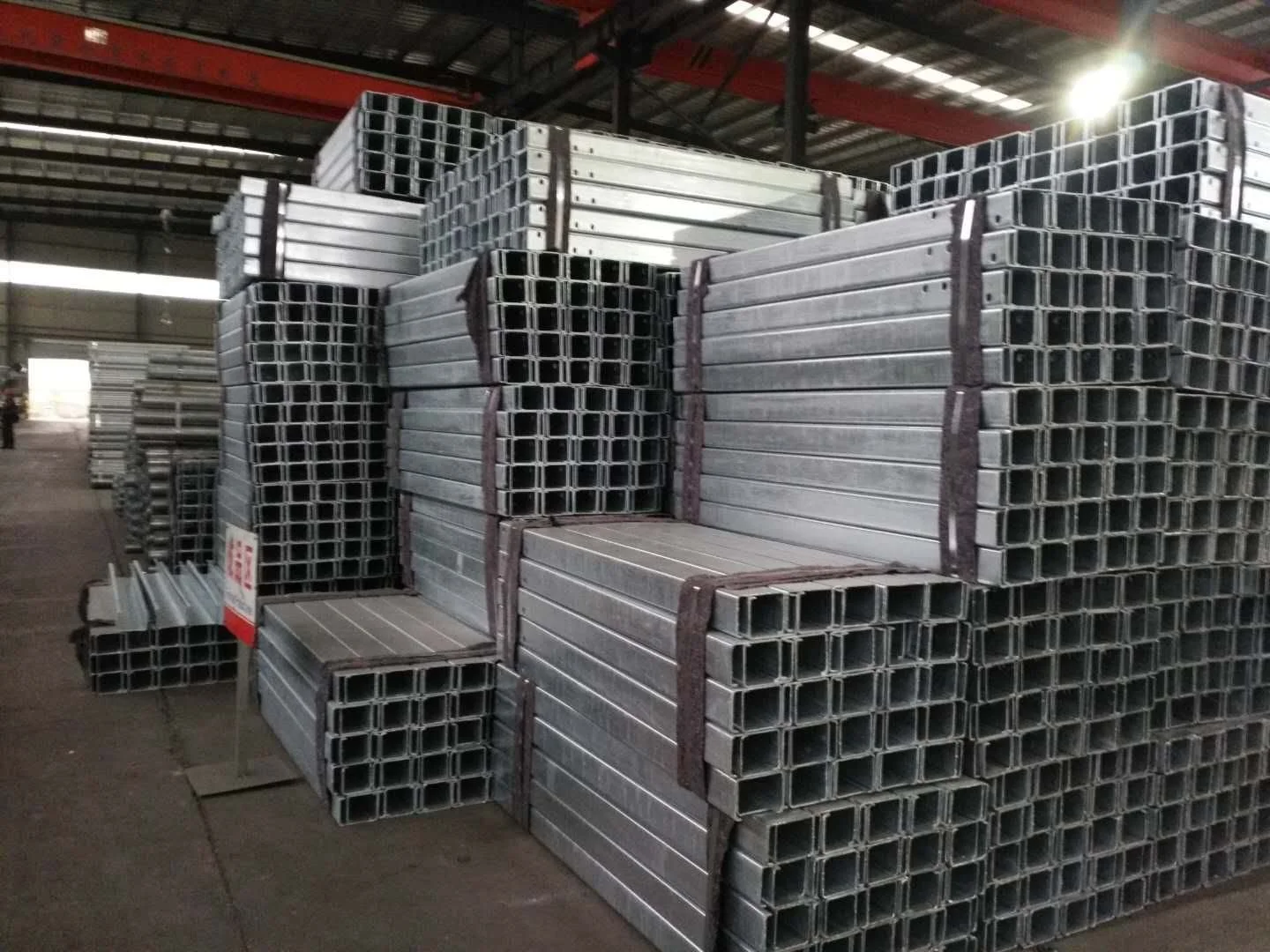 Stacks of metal square hollow pipes stored on pallets in an industrial warehouse.