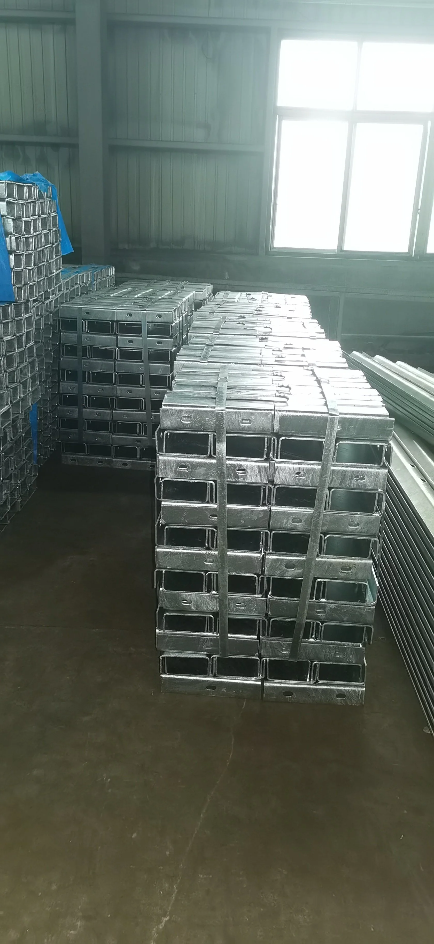 Stacked metal parts in a storage room with metal walls and a window.