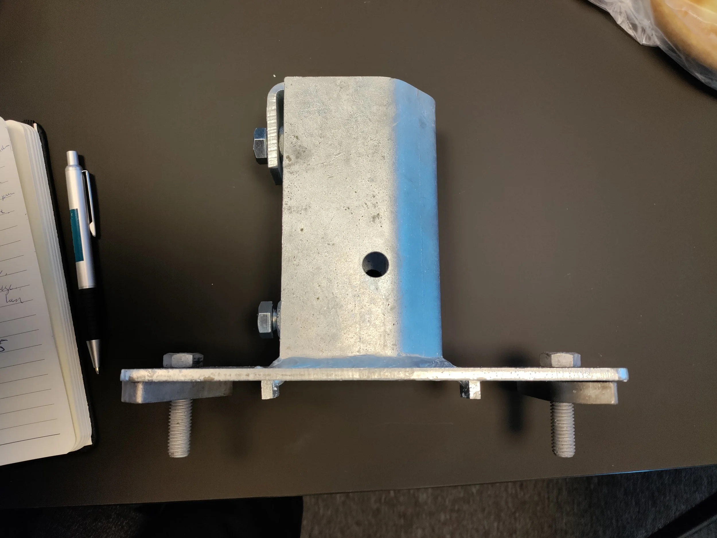 Metal mechanical component with bolts on a flat surface, next to a notebook and pen.