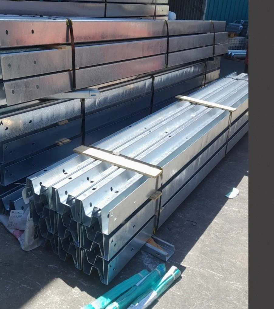 Stacked metal beams and construction materials secured with black straps on an outdoor industrial site.