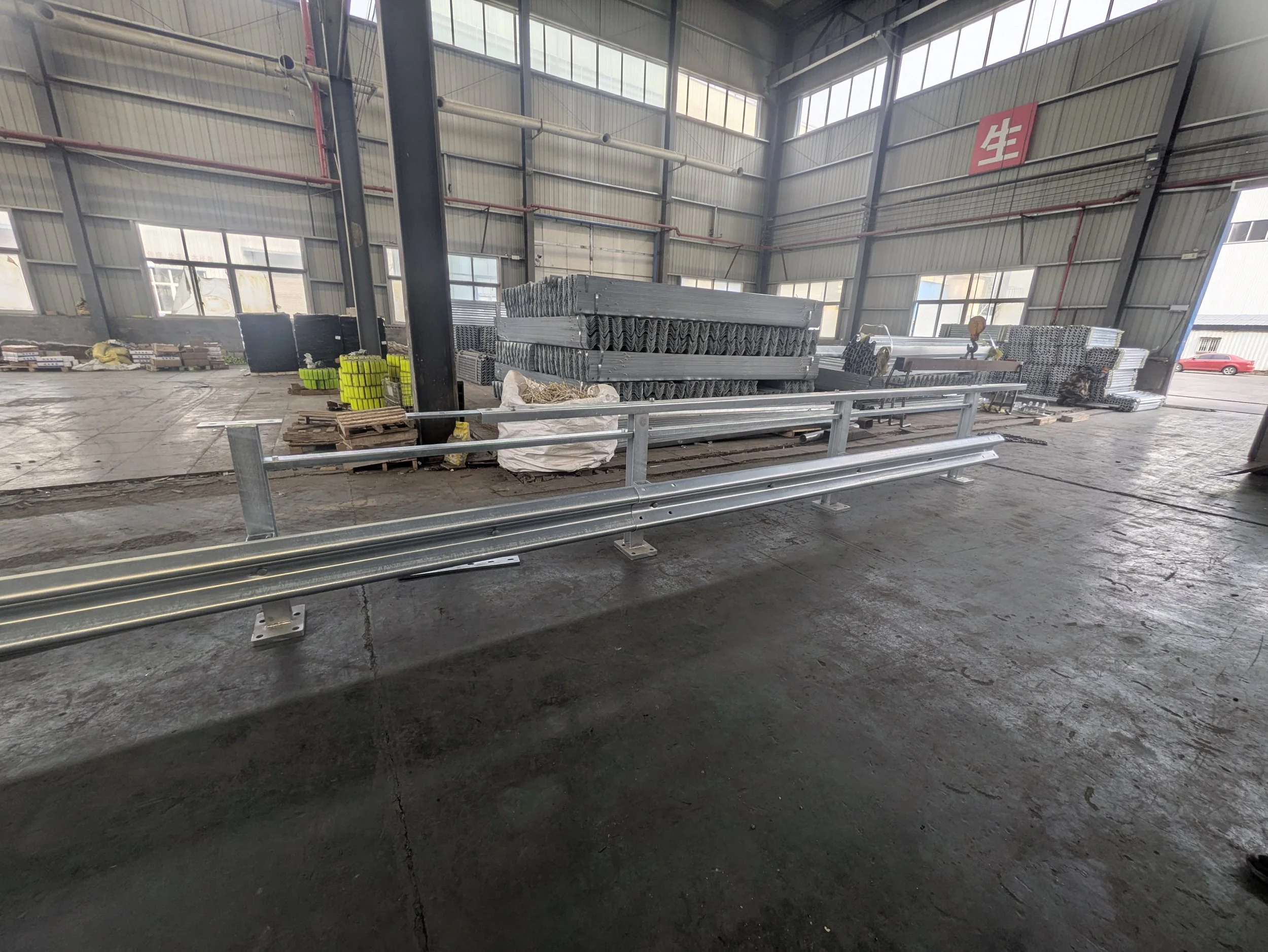 Interior of a manufacturing or warehouse facility with metal scaffolding and stacks of metal pipes, equipment, and supplies arranged around the space. There is a red sign with white characters on the wall.