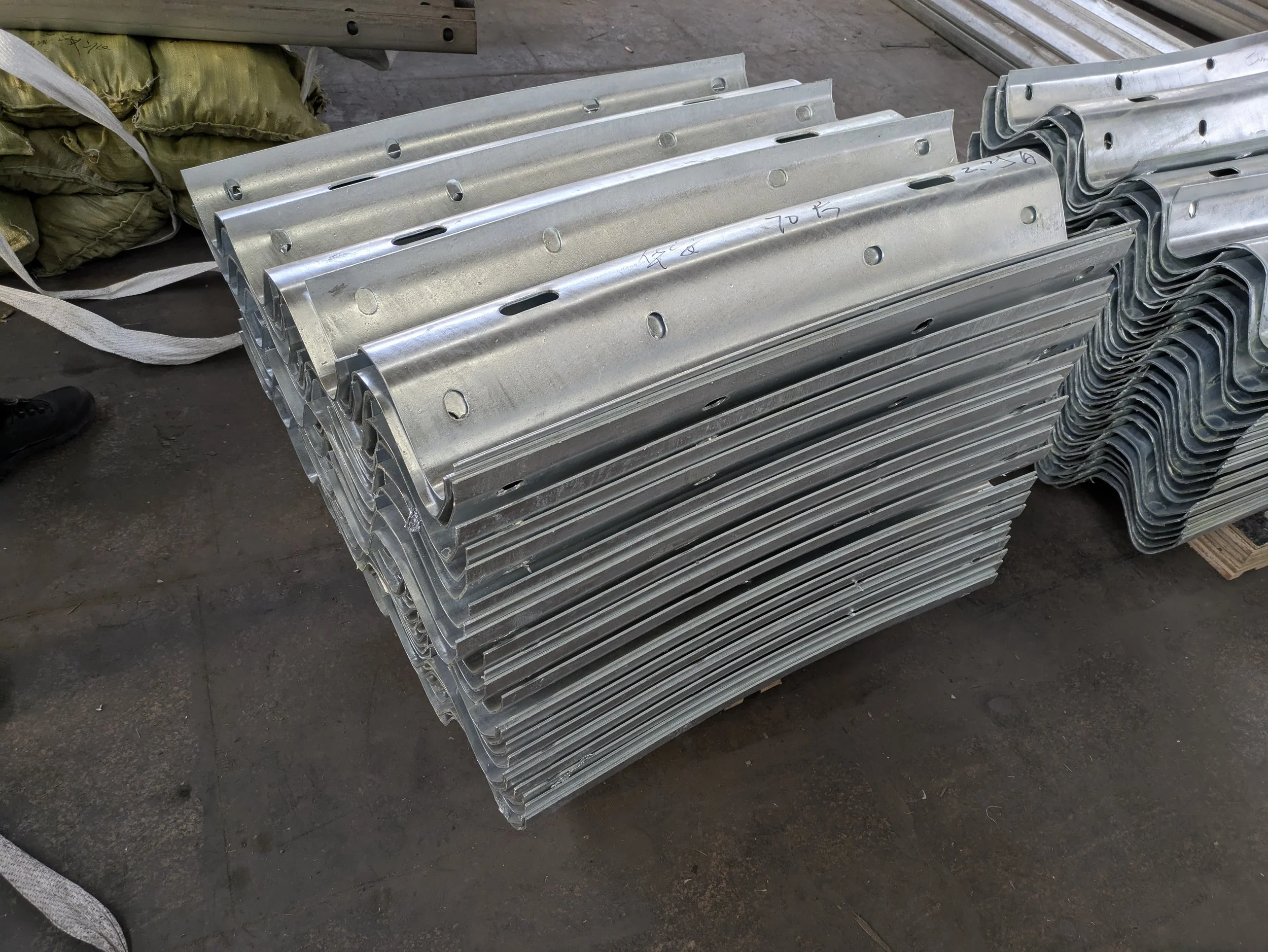 Stacked metal brackets with multiple holes, placed on a concrete floor in an industrial setting.