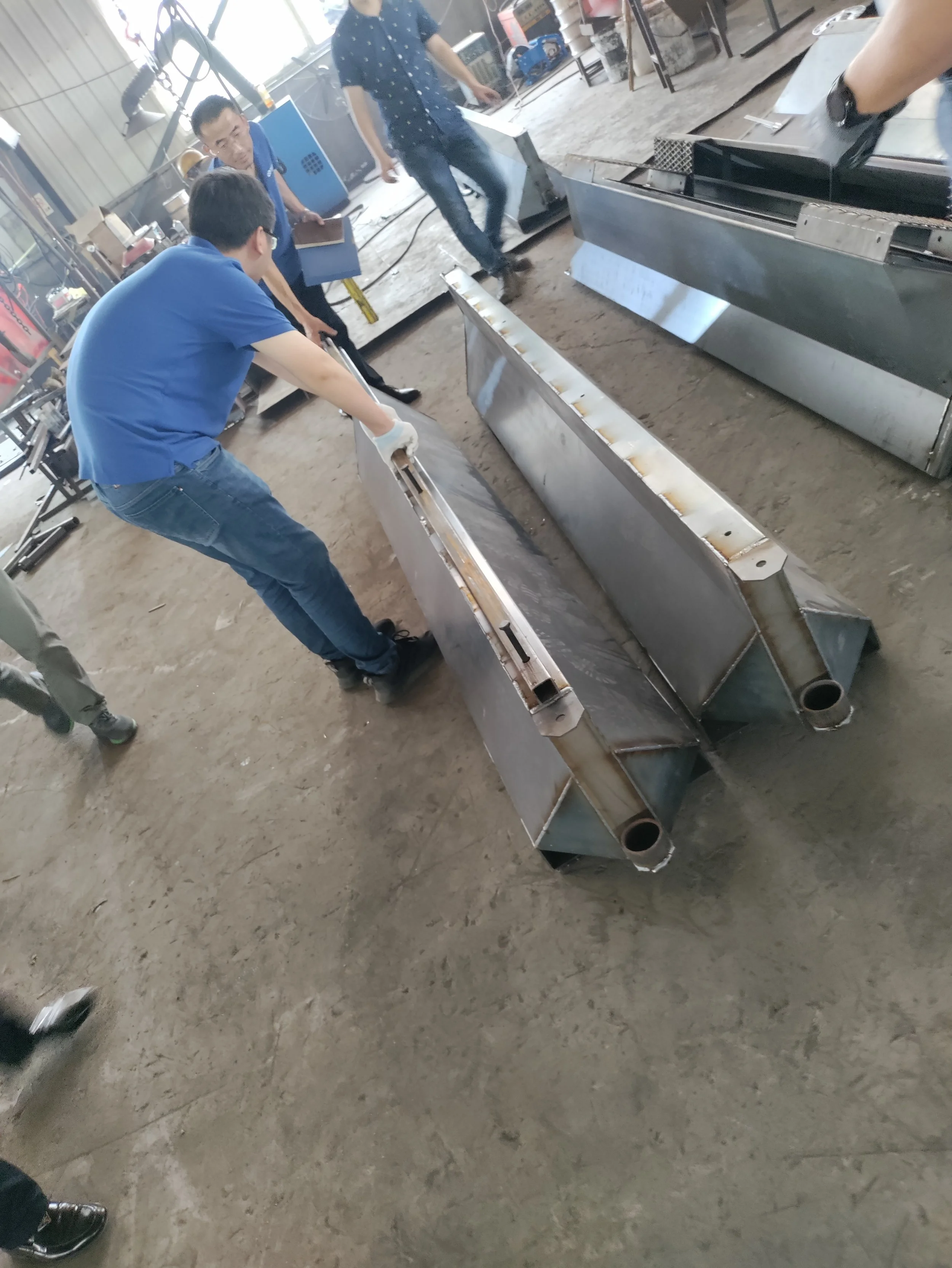 People working on large metal duct components in a workshop or manufacturing area.