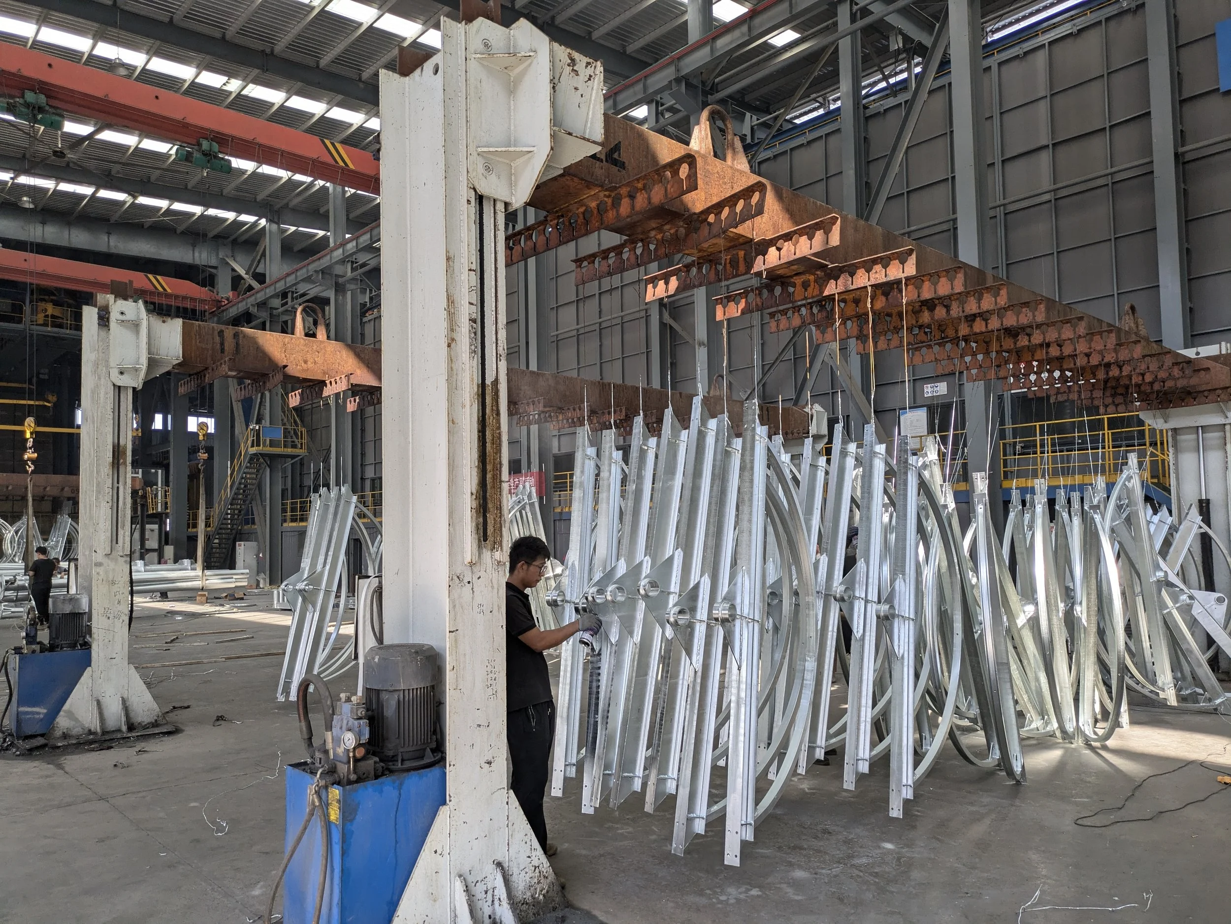Inside a factory with metal structures and workers, metal frames hanging and being assembled.