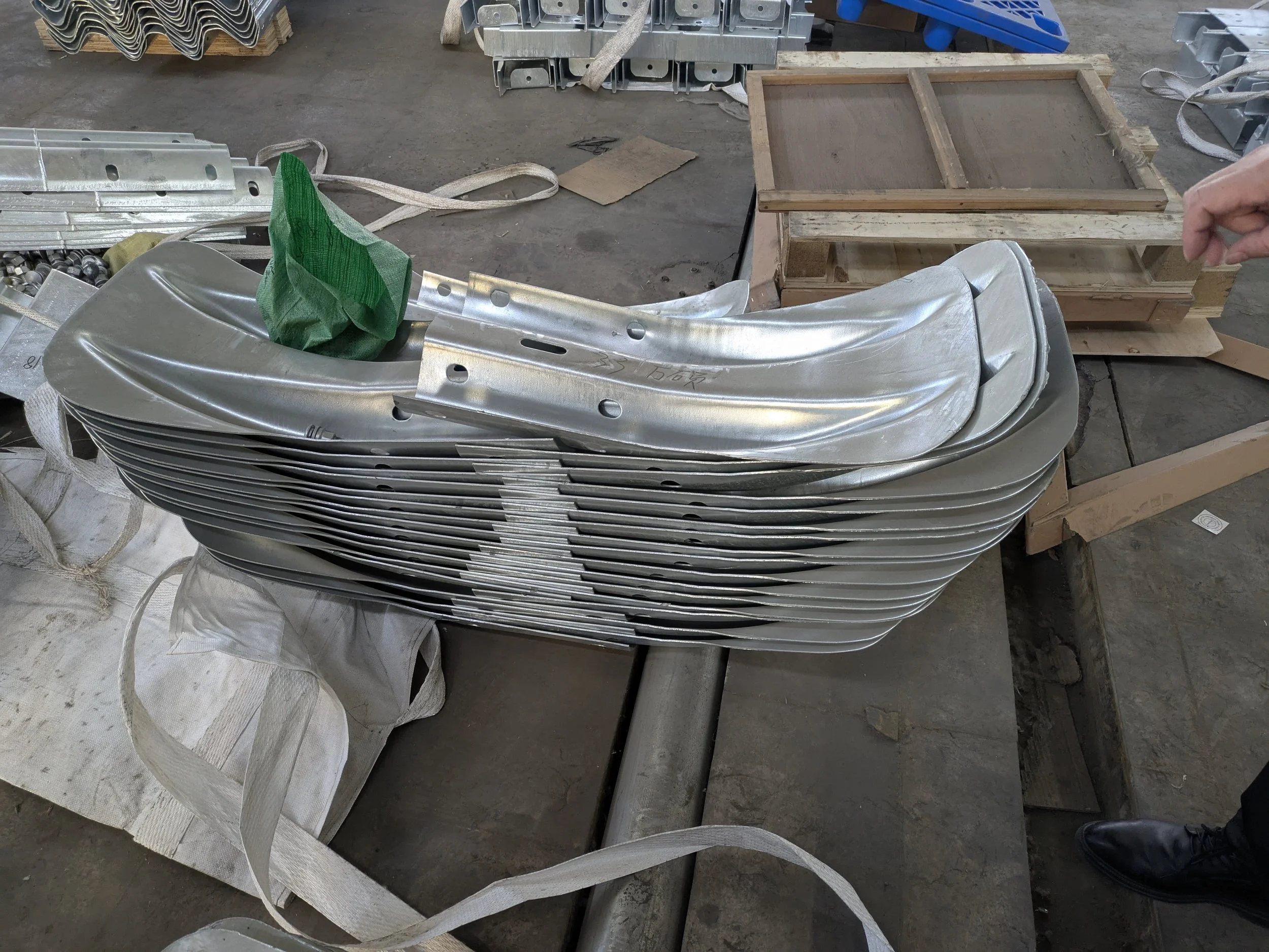 Stacked aluminum or metal parts in a factory setting, with workbench, tools, and wooden crates in the background.