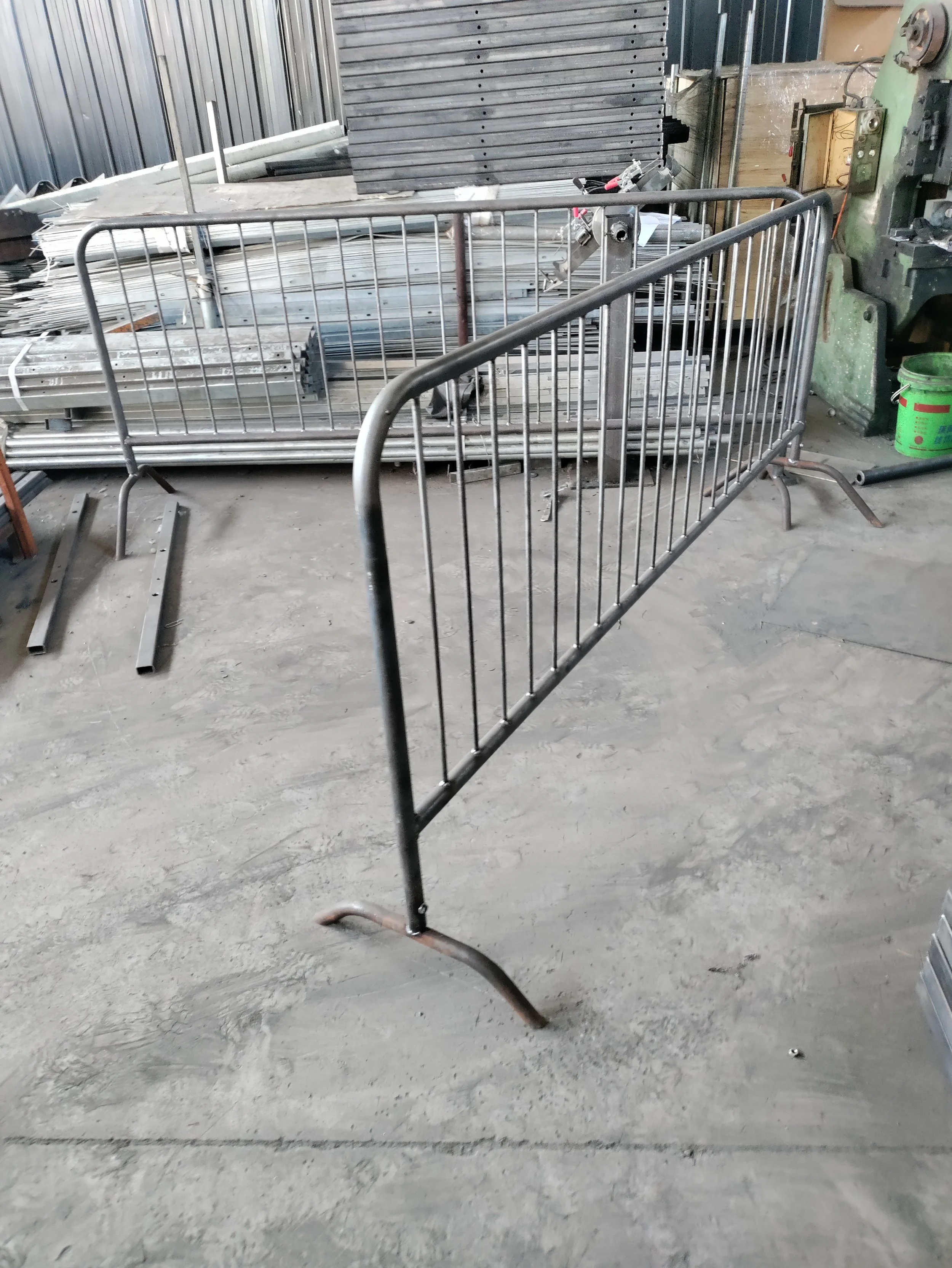 Empty metal safety barrier in an industrial workshop with metal shelves, tools, and equipment in the background.