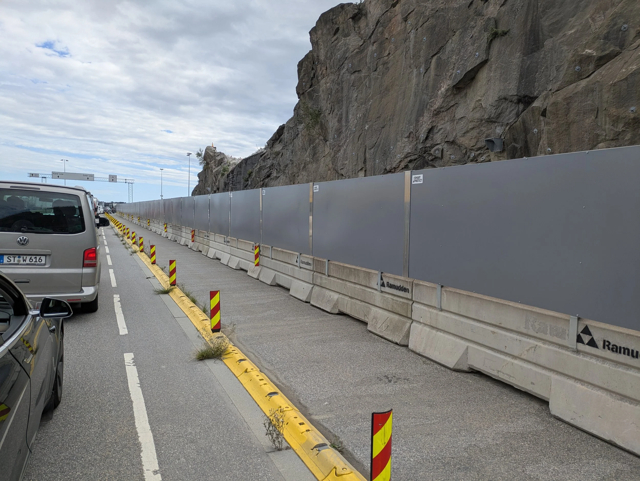 Construction barriers and wall along a road next to a rocky hillside, with vehicles stopped in traffic.