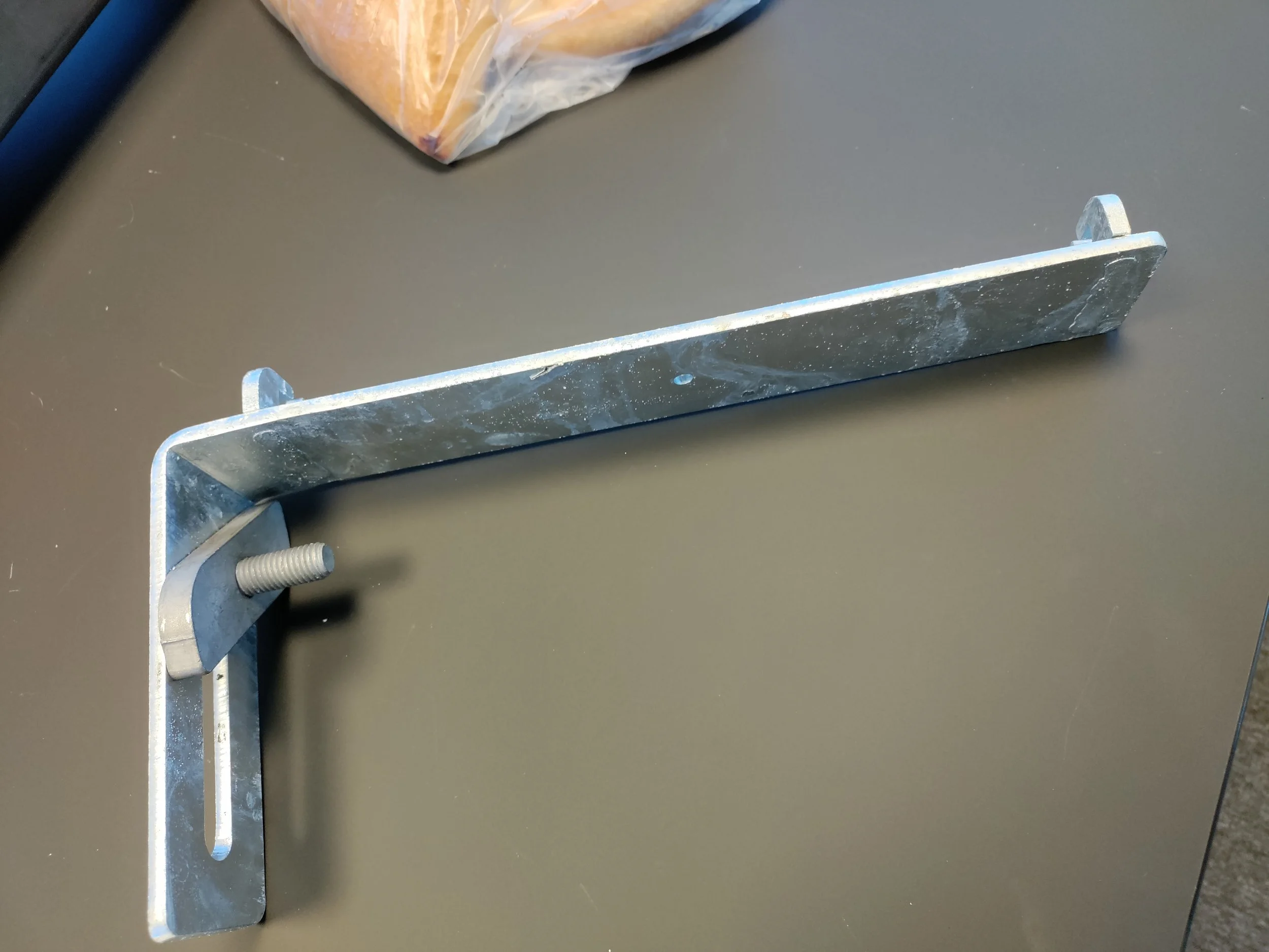 A metal L-shaped bracket with a threaded bolt and a wing nut, placed on a gray surface.