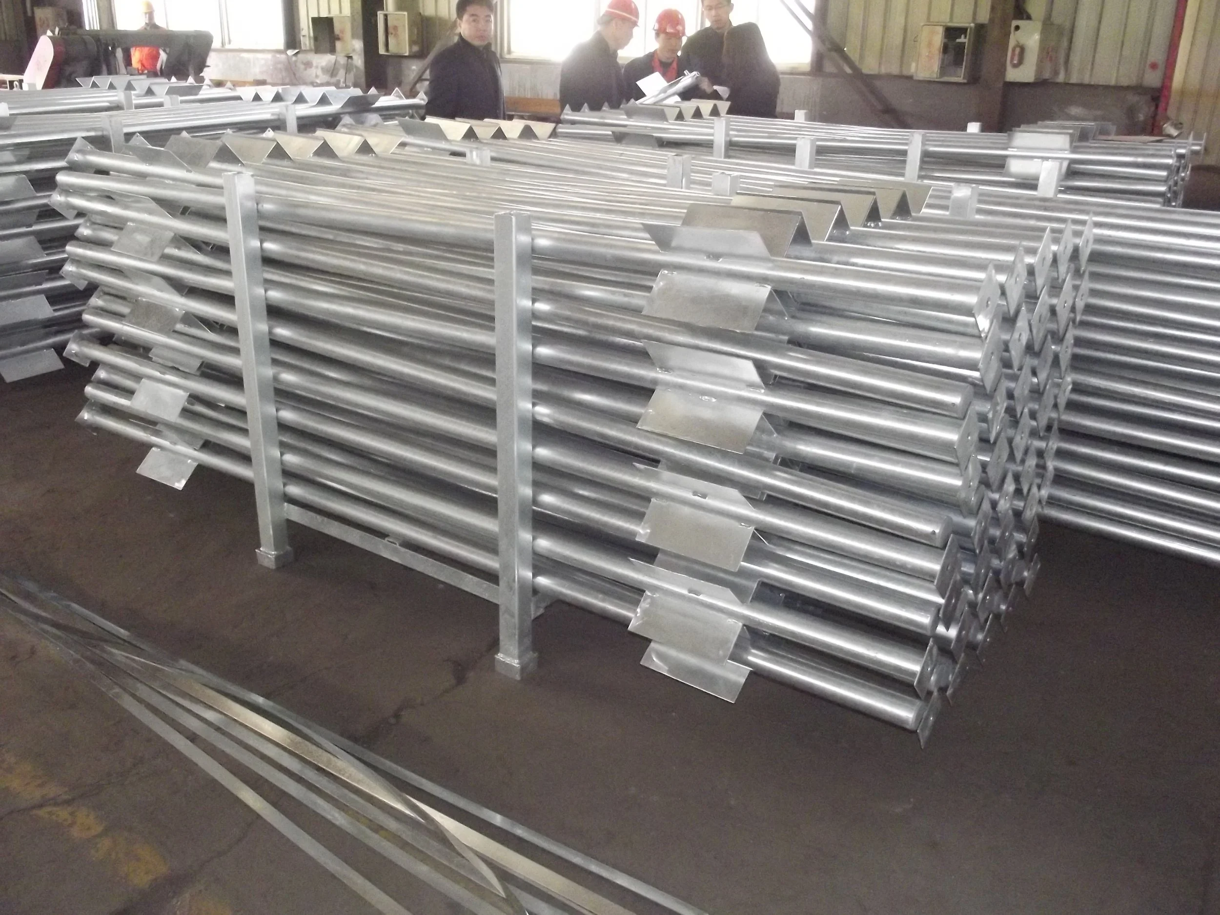 Stacked metal pipes on a warehouse floor with people in the background.