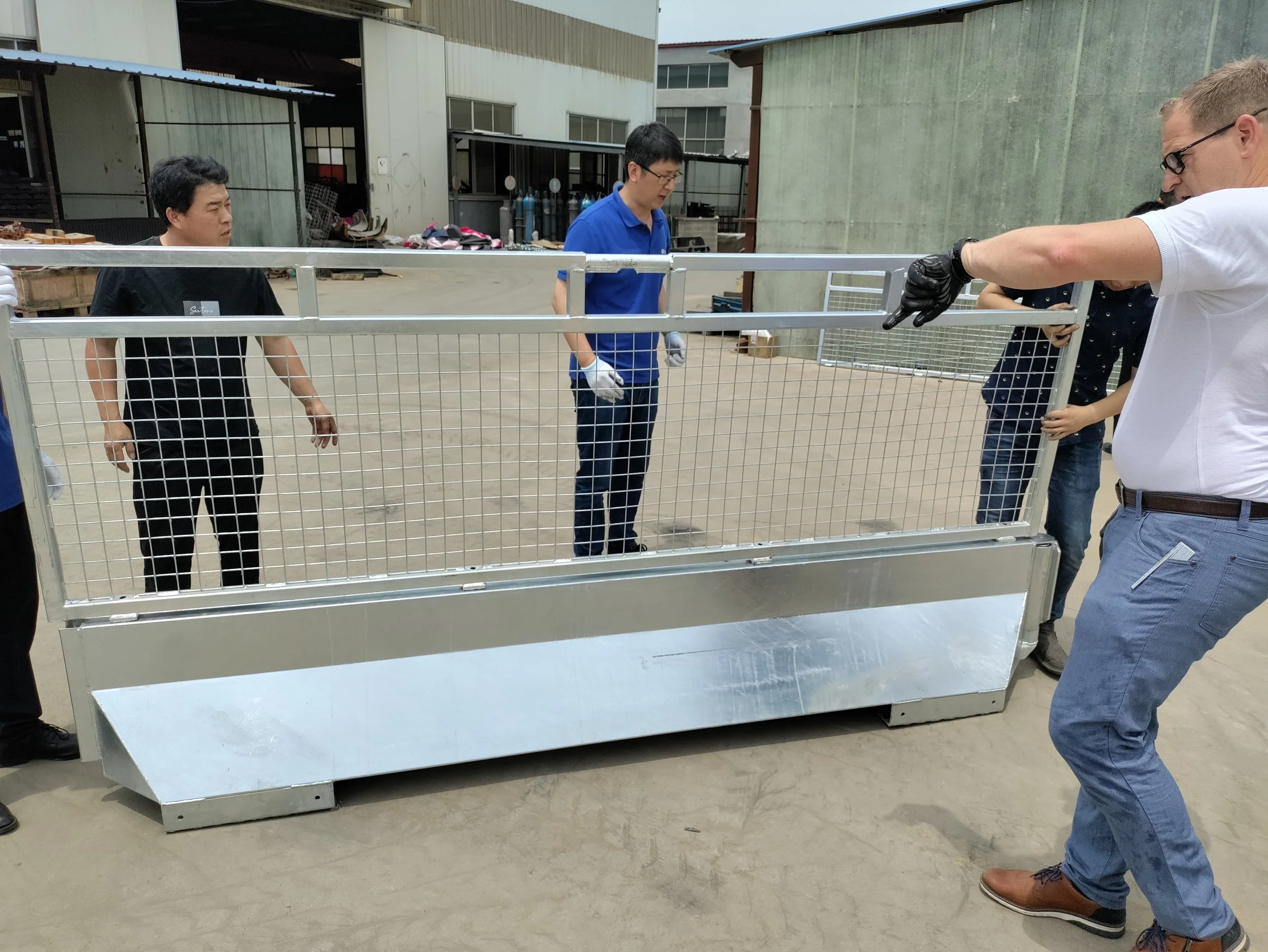 People assembling a metal and wire animal transport trailer outdoors on concrete ground.