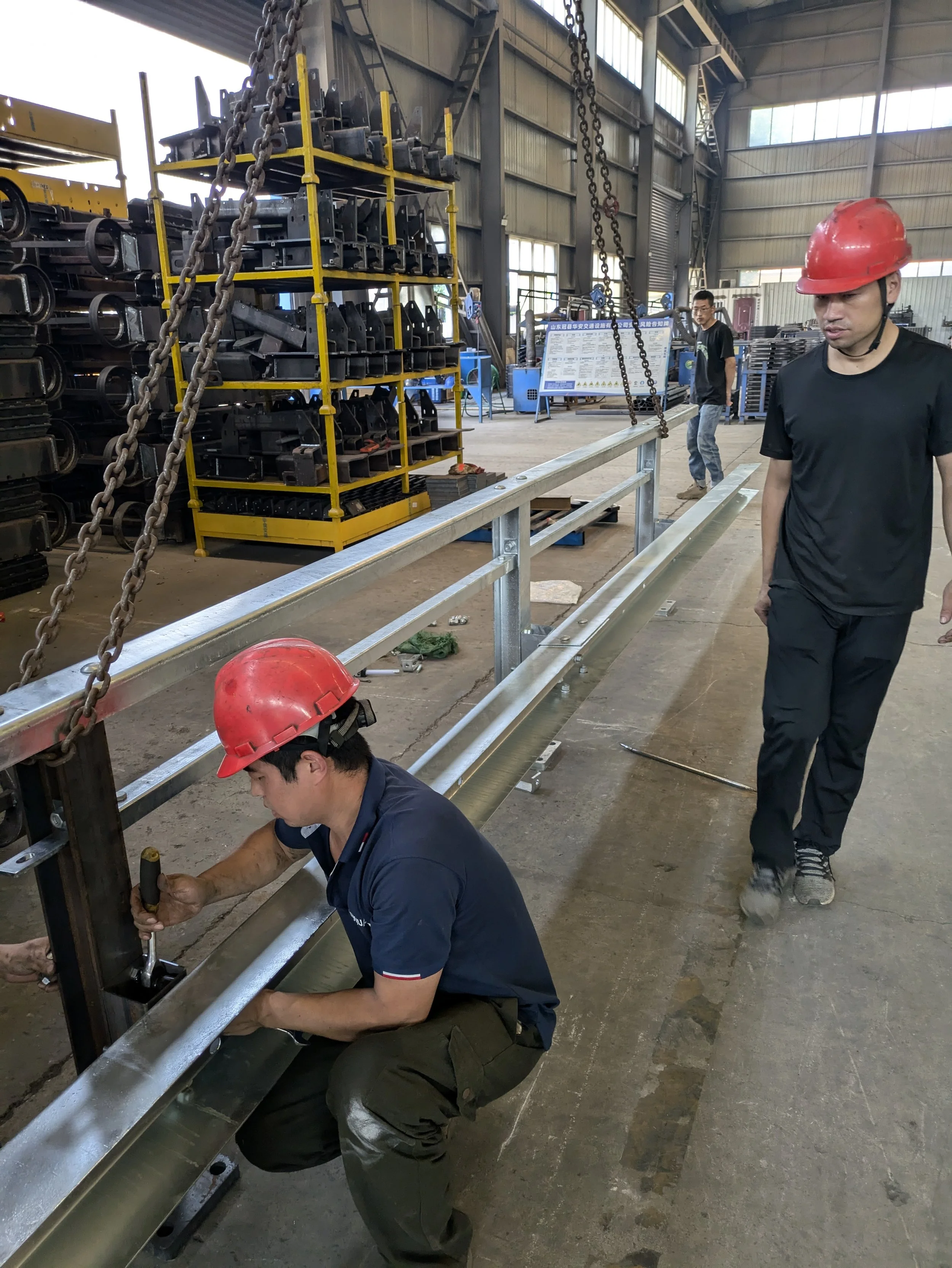 Workers with red helmets assembling metal framework in a factory.