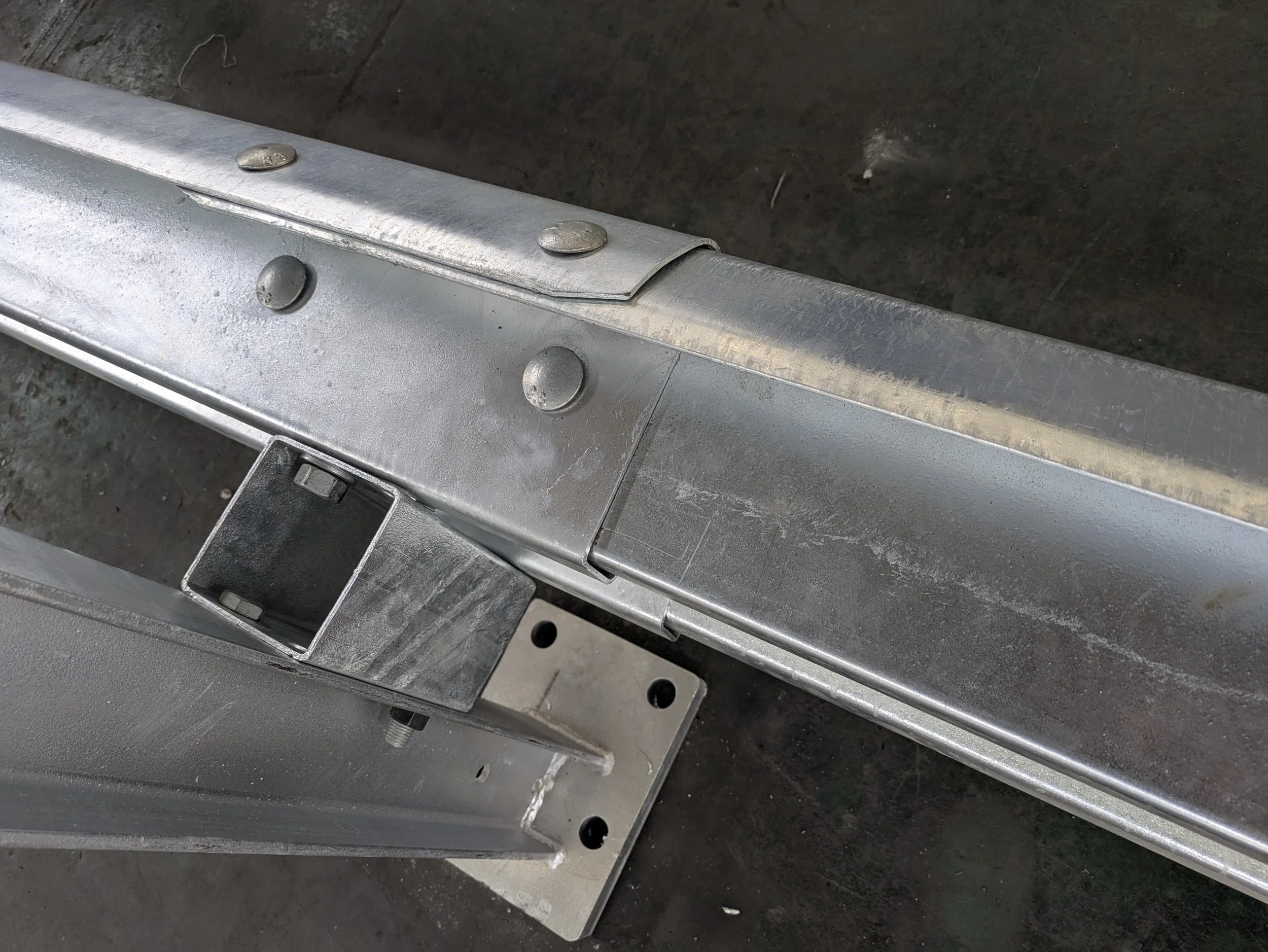 Close-up of a metal frame or structure, showing rivets and a square metal piece attached, with a dark background.