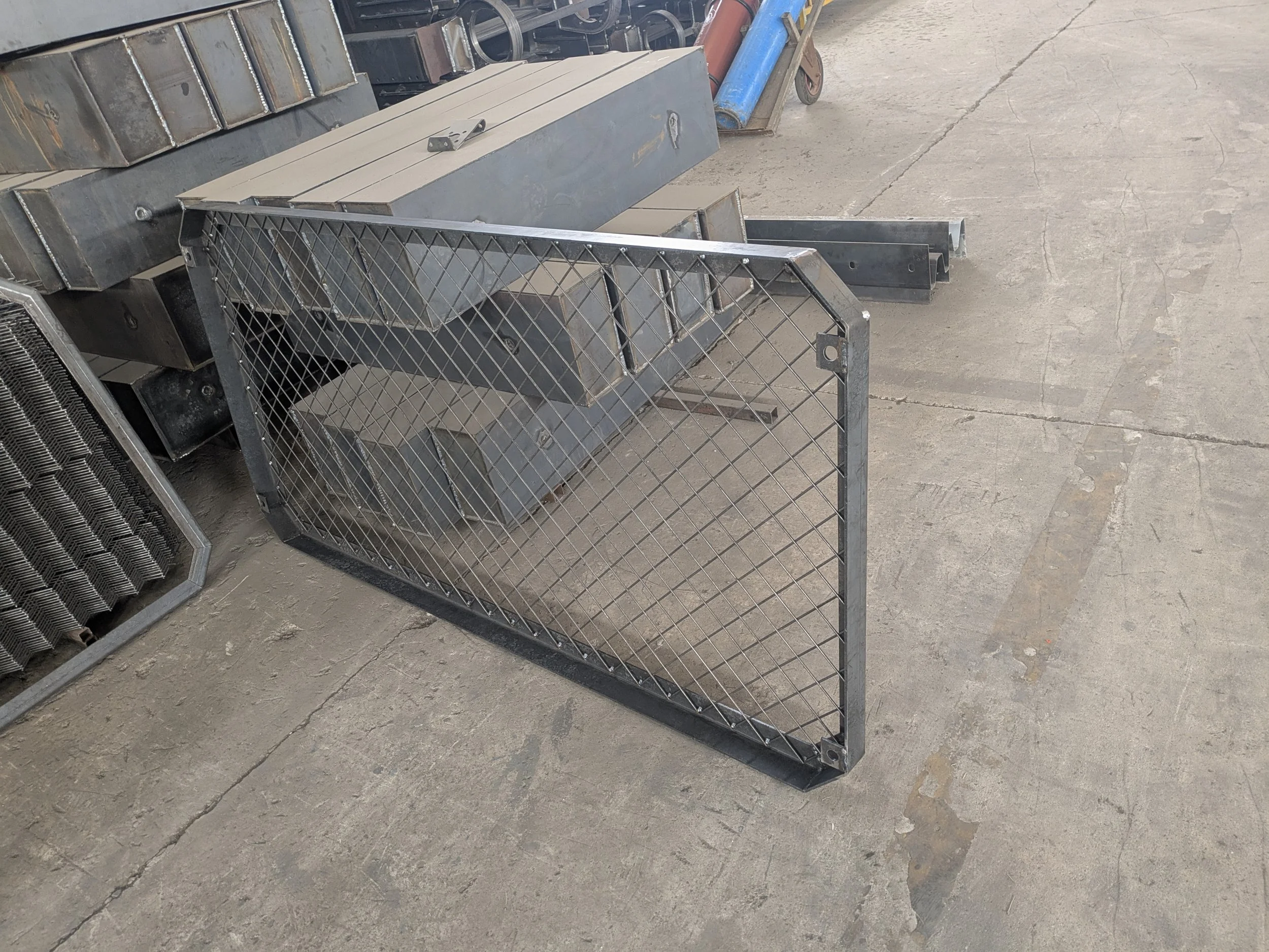 Metal fence panel leaning on a concrete floor, with industrial equipment and tools in the background.