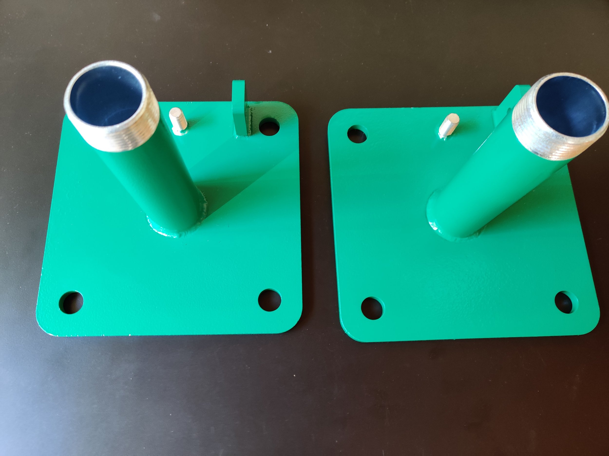 Two green metal plates with cylindrical tubes attached, placed on a black surface.