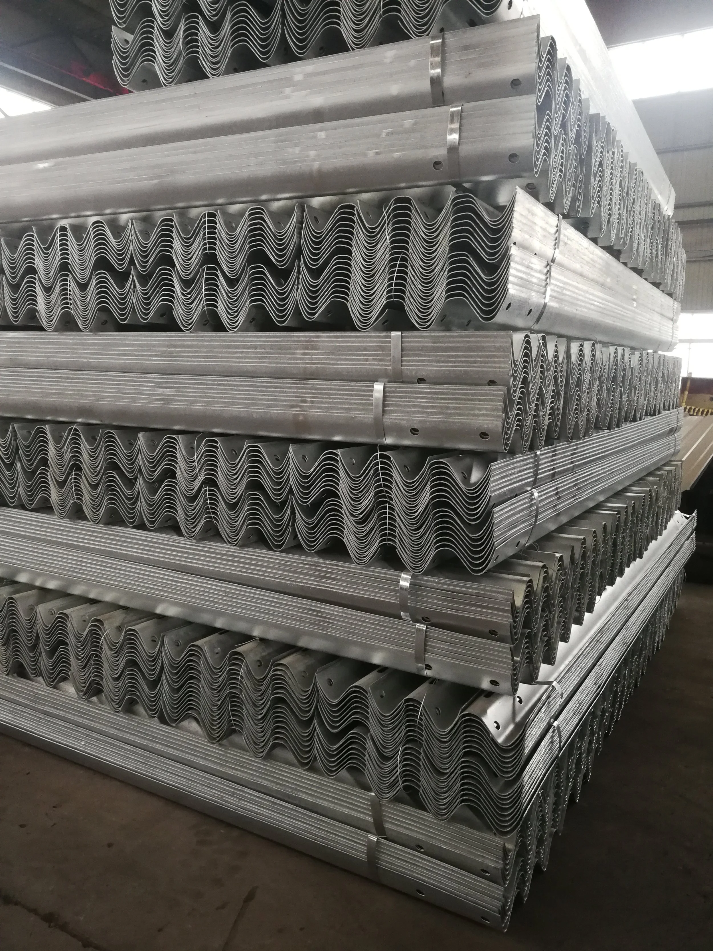 Piles of stacked metal angle bars with holes, stored in an industrial warehouse.