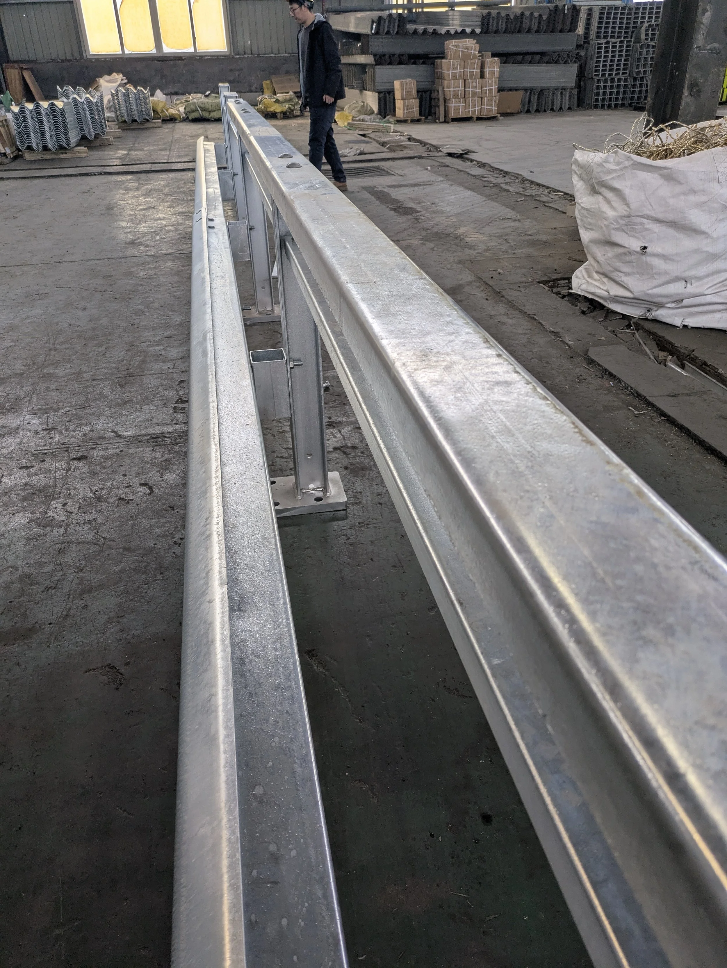 Metal guardrail in an industrial warehouse with a person walking in the background.