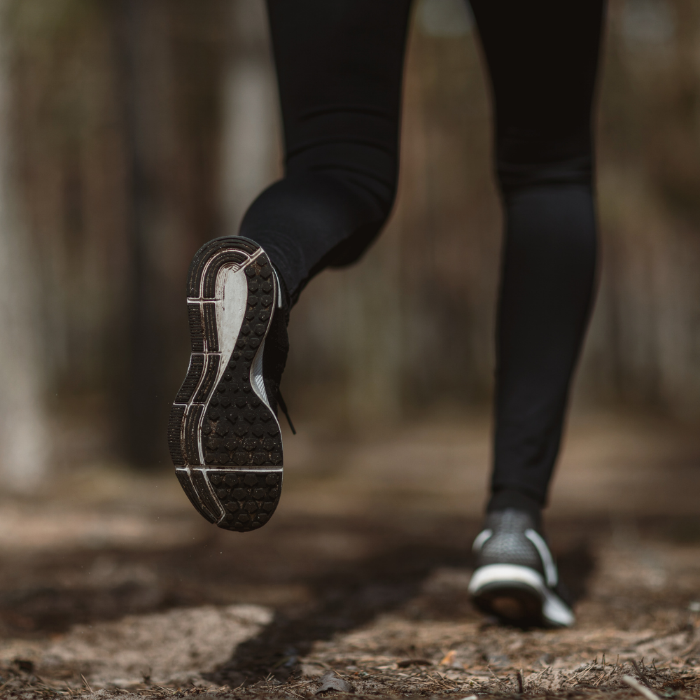 Person running outdoors, focusing on their black athletic shoes and black pants.