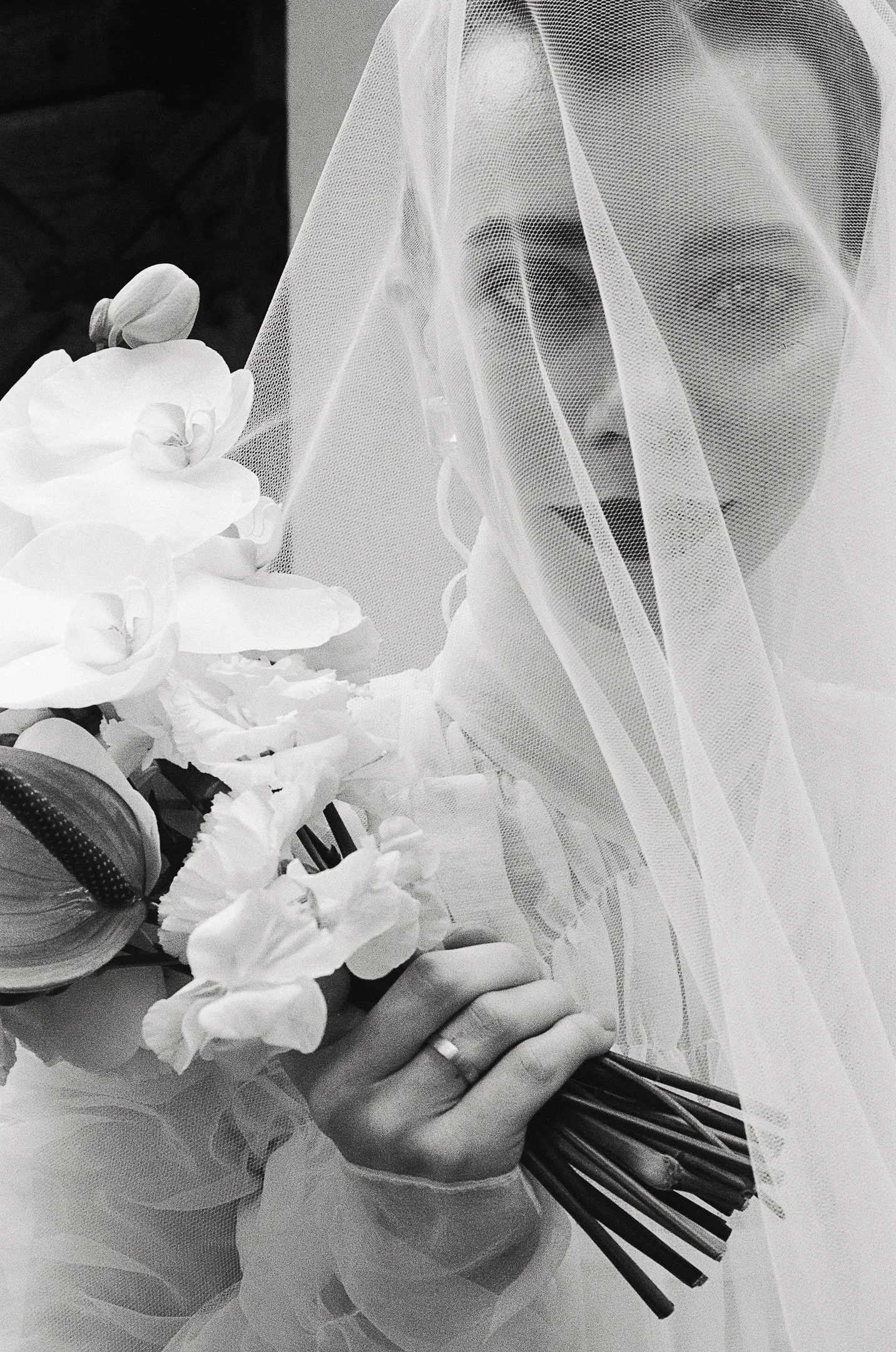 A black and white photo of a woman in a wedding veil holding a bouquet of flowers, partially obscuring her face.