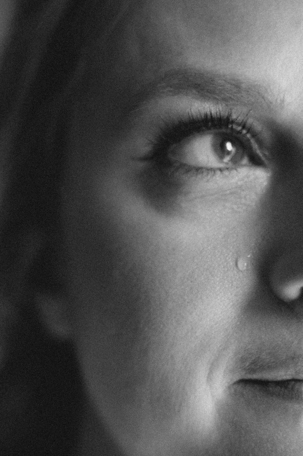 Close-up of a woman's face in black and white, focusing on her eye with a tear rolling down her cheek.