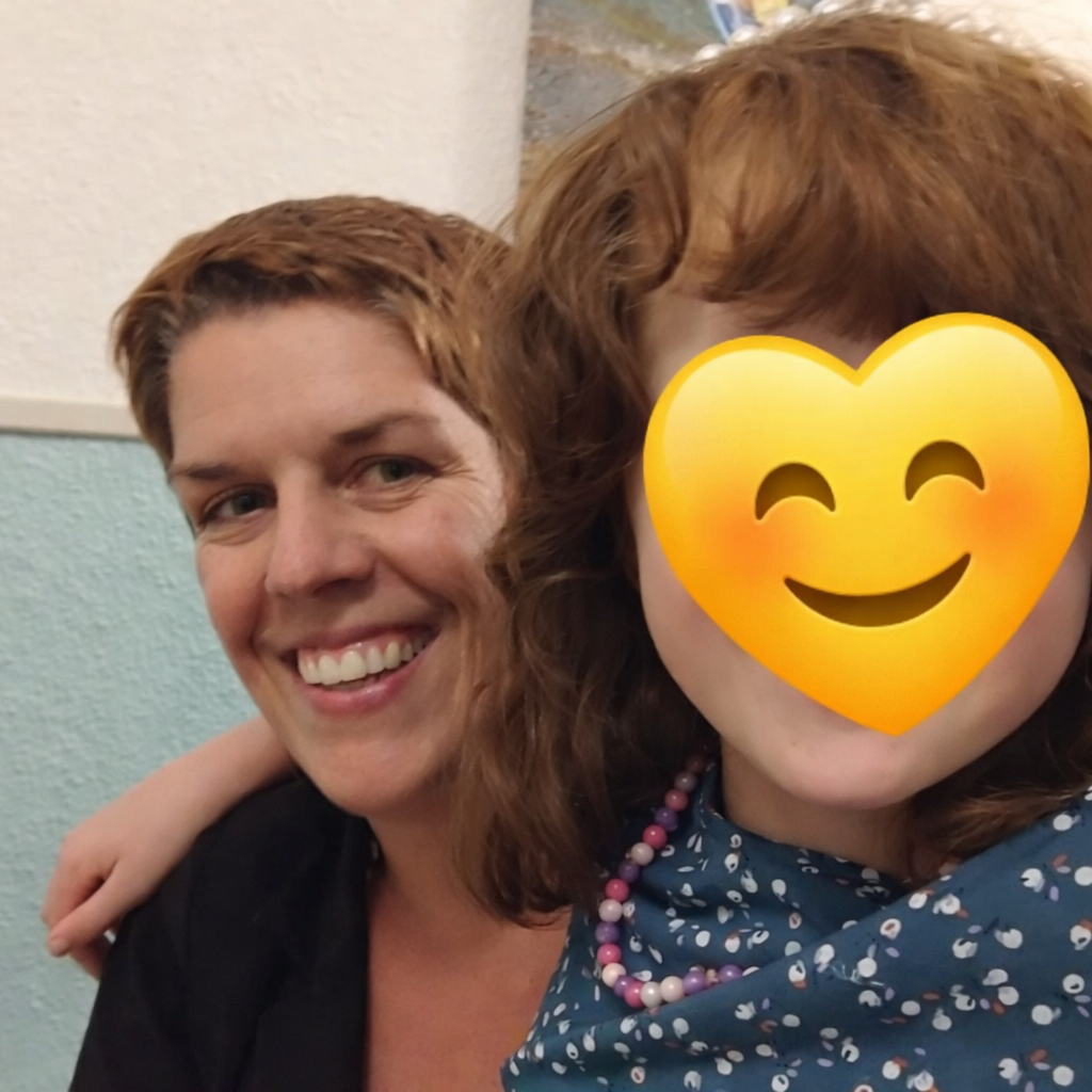 Zwei Frauen, eine lächelnd, die andere mit einem lachenden Emoji im Gesicht, in einem Raum mit hellblauen Wänden.