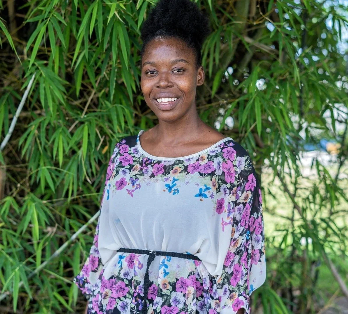 Young Haitian woman smiling outside in front of greenery with a floral shirt on