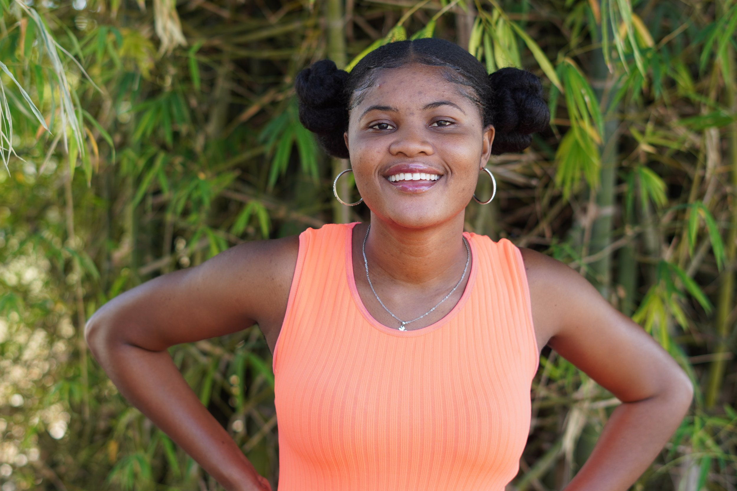 Young Haitian woman smiles with her hands on her hips in front of greenery