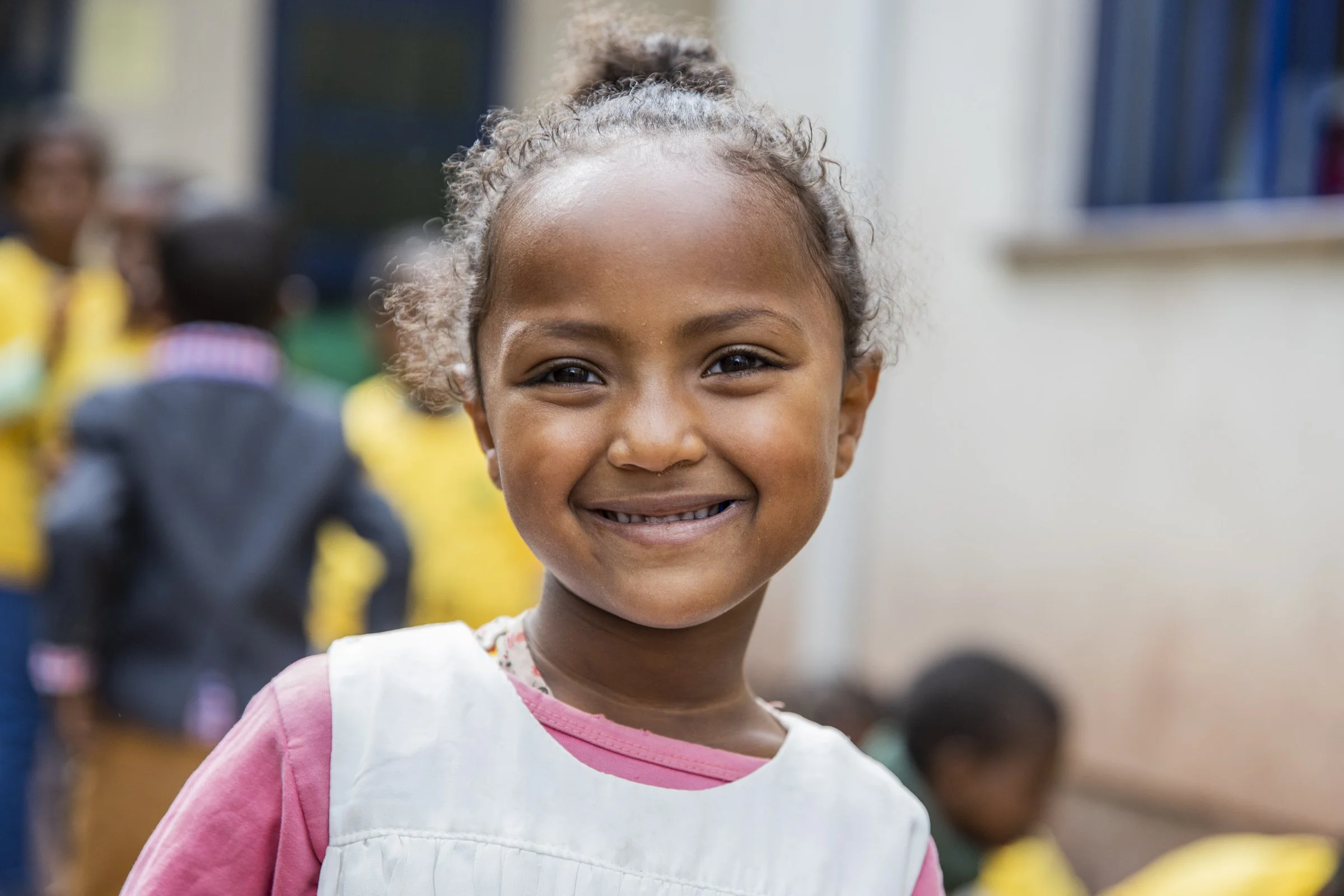Little Ethiopian girl smiles as other children play in the background
