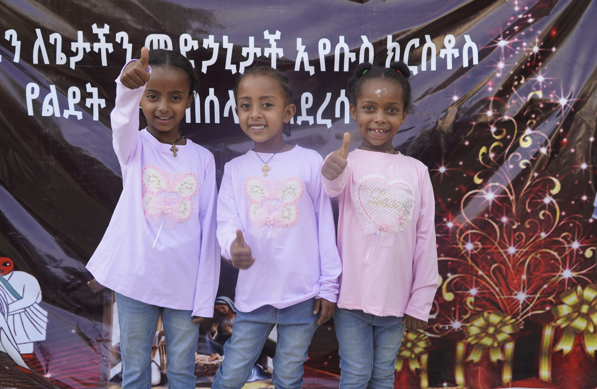 Three little girls smile in matching shirts and give thumbs-ups