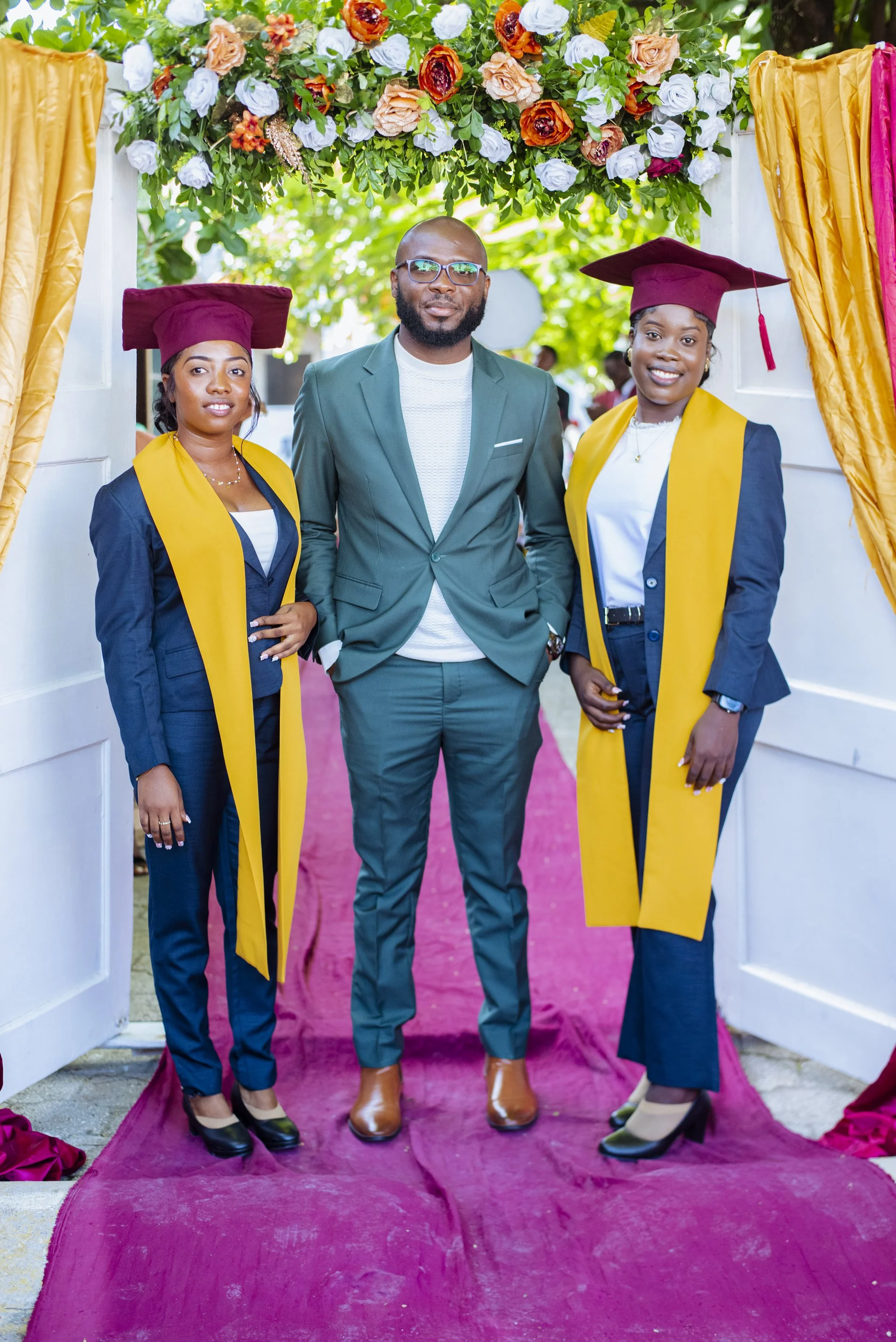 Two young Haitian women in caps and gowns smiling with their past instructor