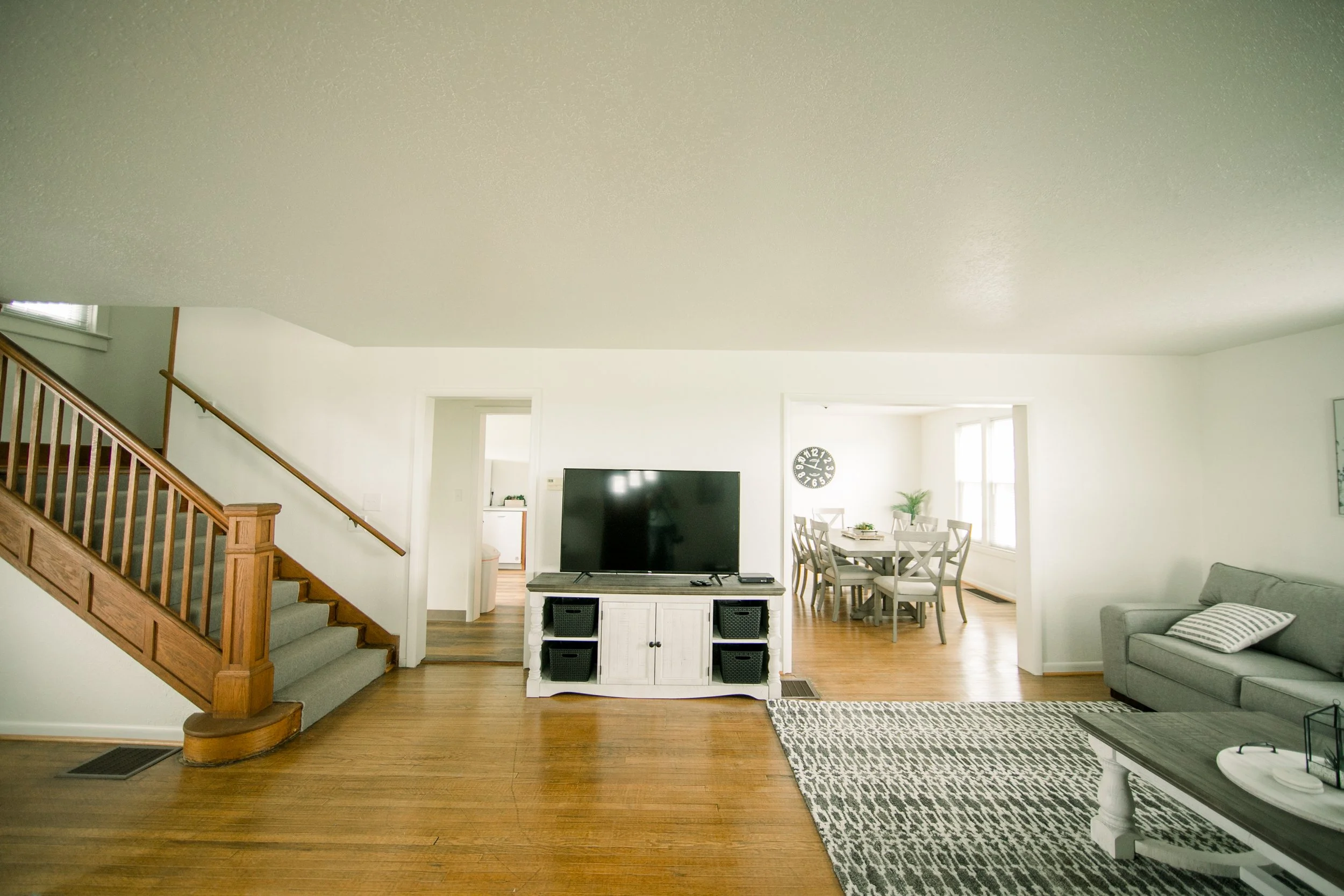 Living room showing stairs leading up, front-view of the TV, and the entrance to the kitchen. 