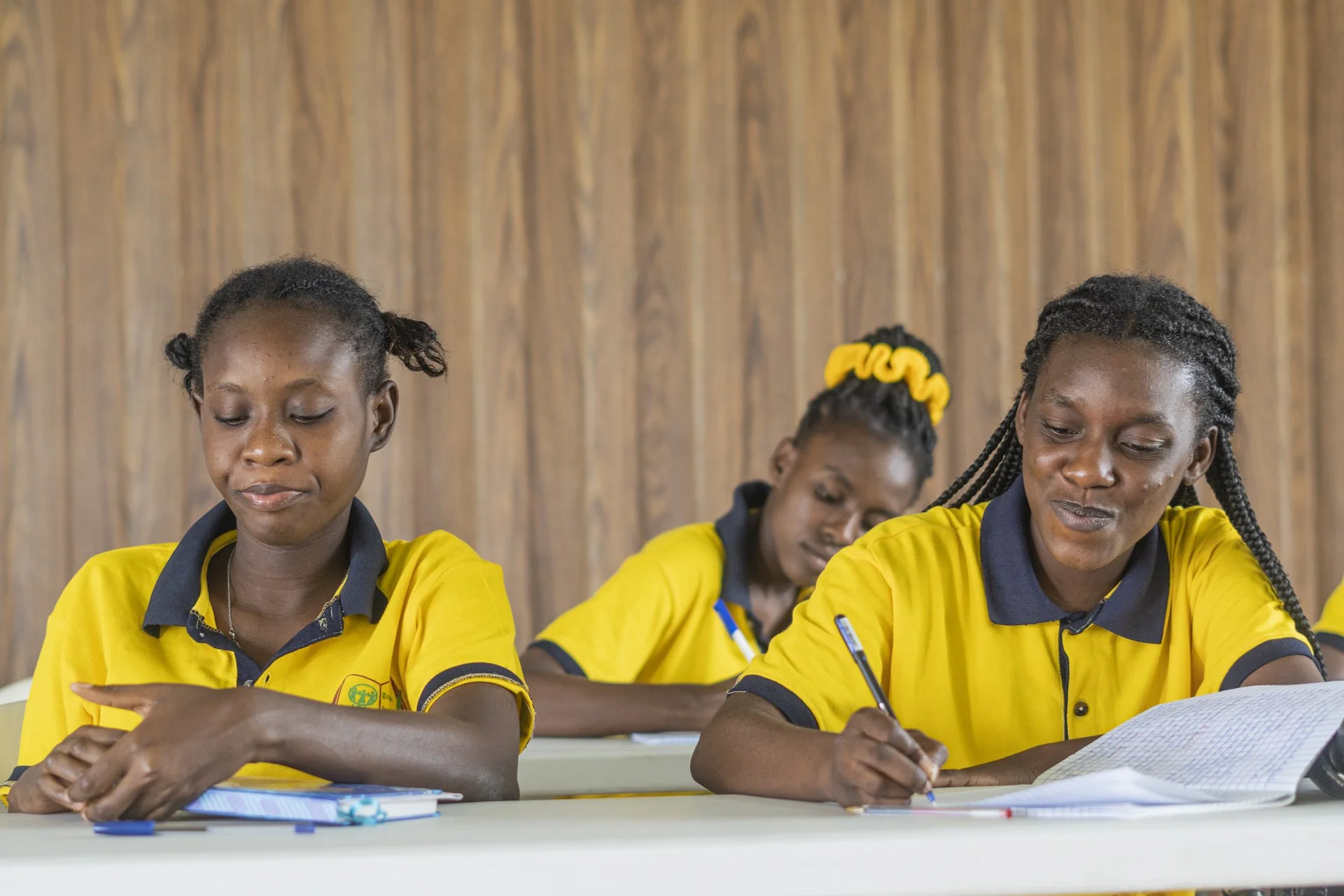 Young Haitian women studying at their desks in a classroom wearing their yellow uniforms