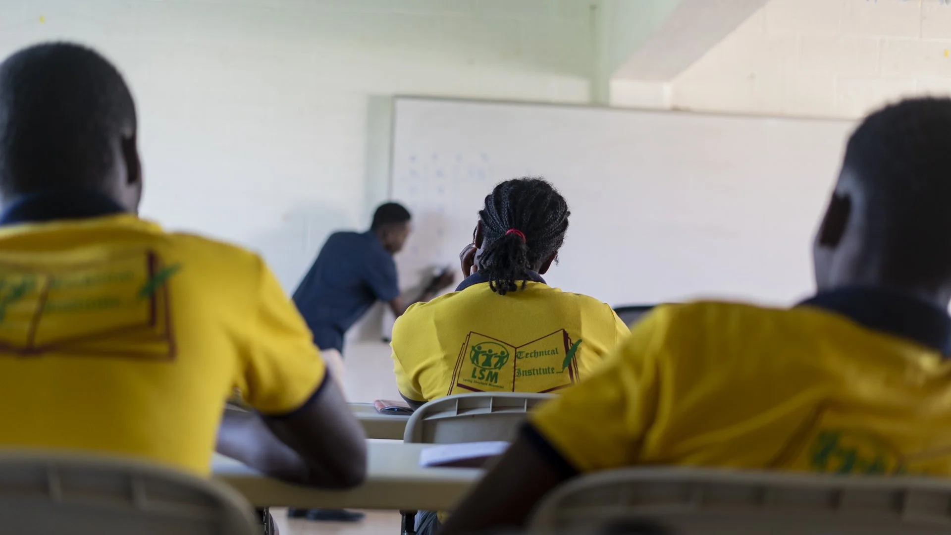 Students listen to their instructor as he writes on the white board