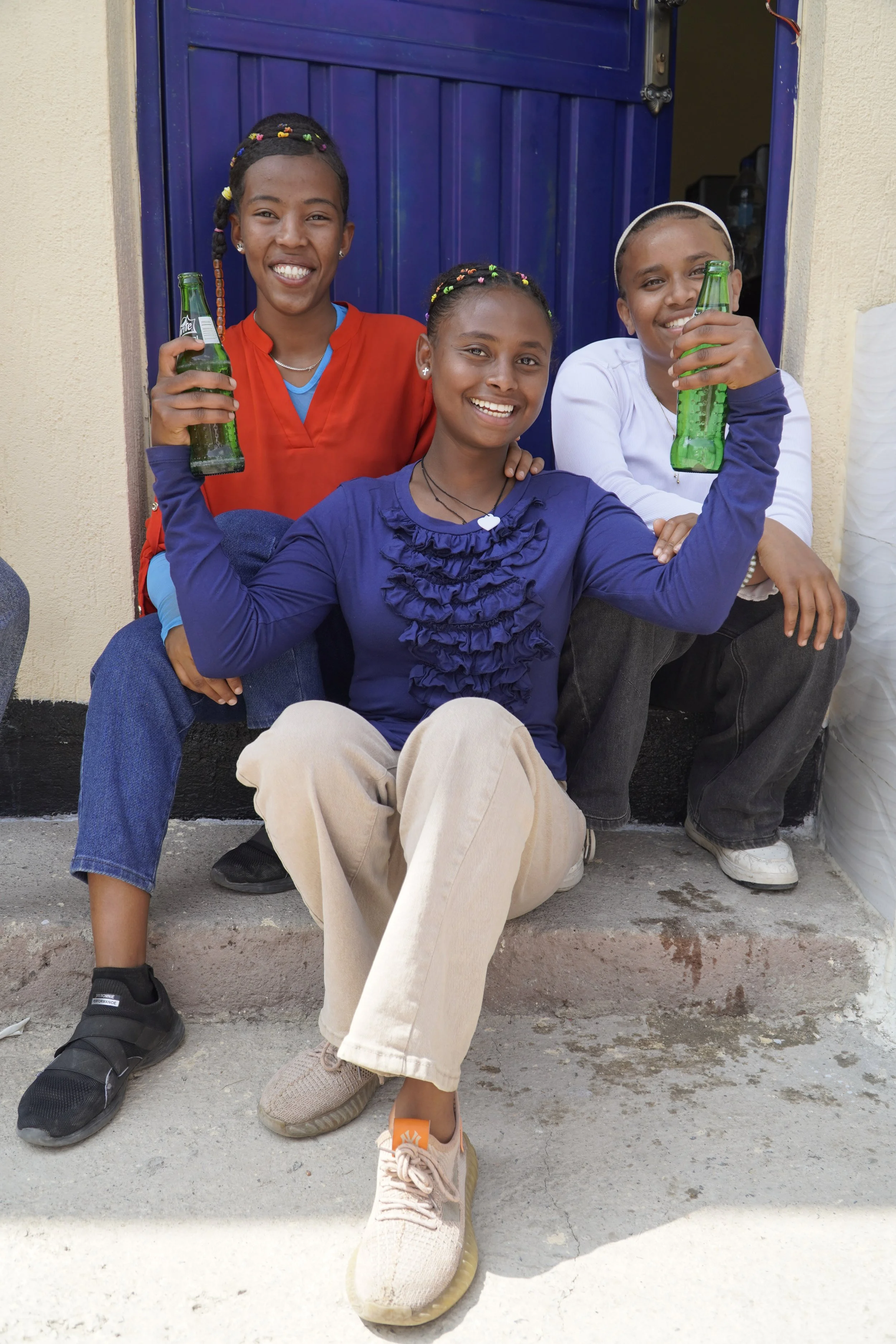 Three young women sitting together and laughing as they hold up their sodas