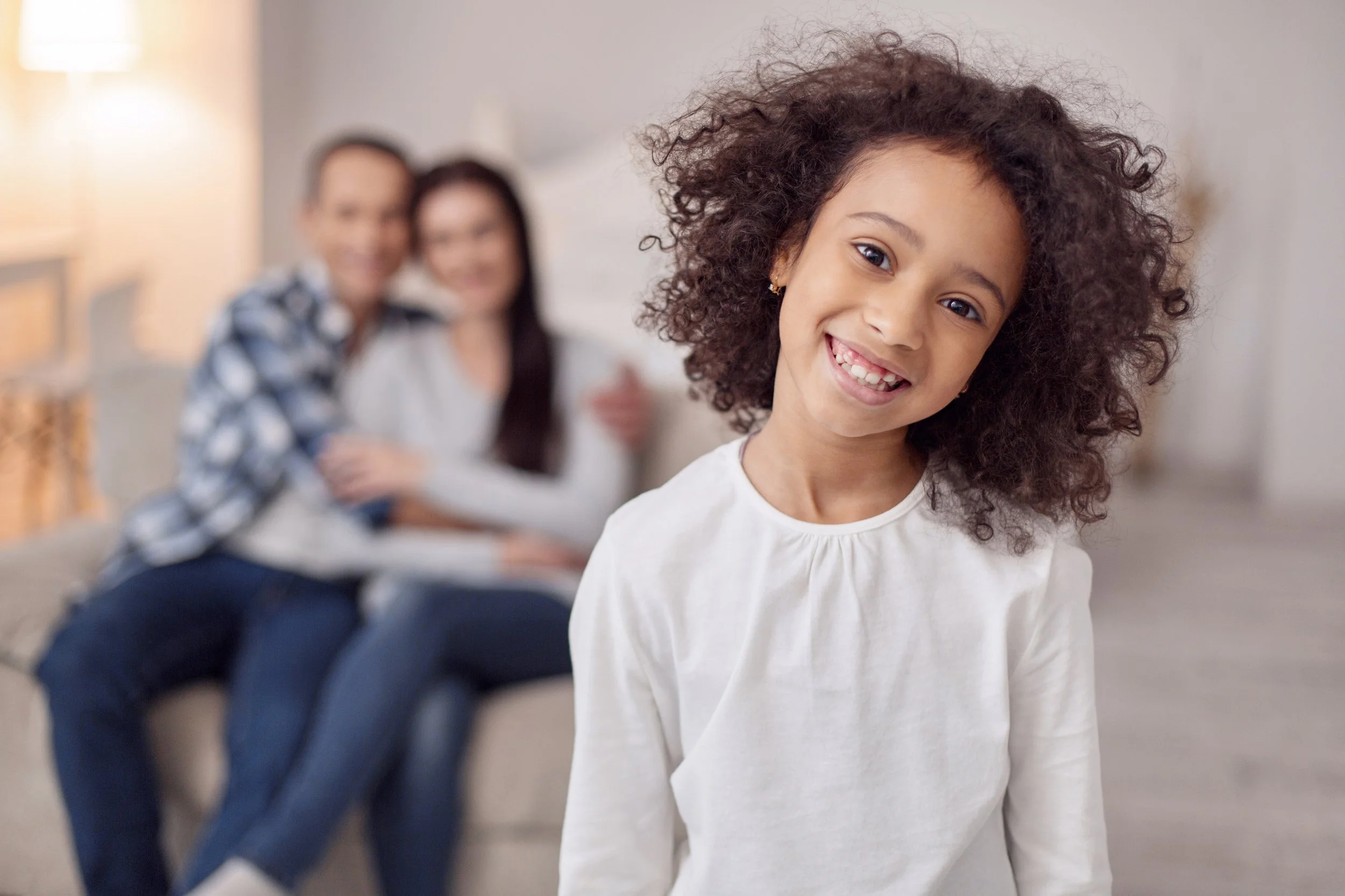 Young girl smiling as her parents smile at her in the background