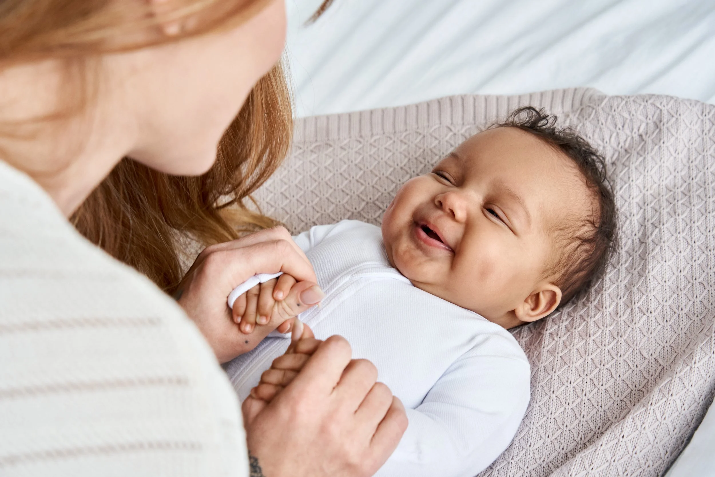 Baby smiling up at his mother who is holding his hands