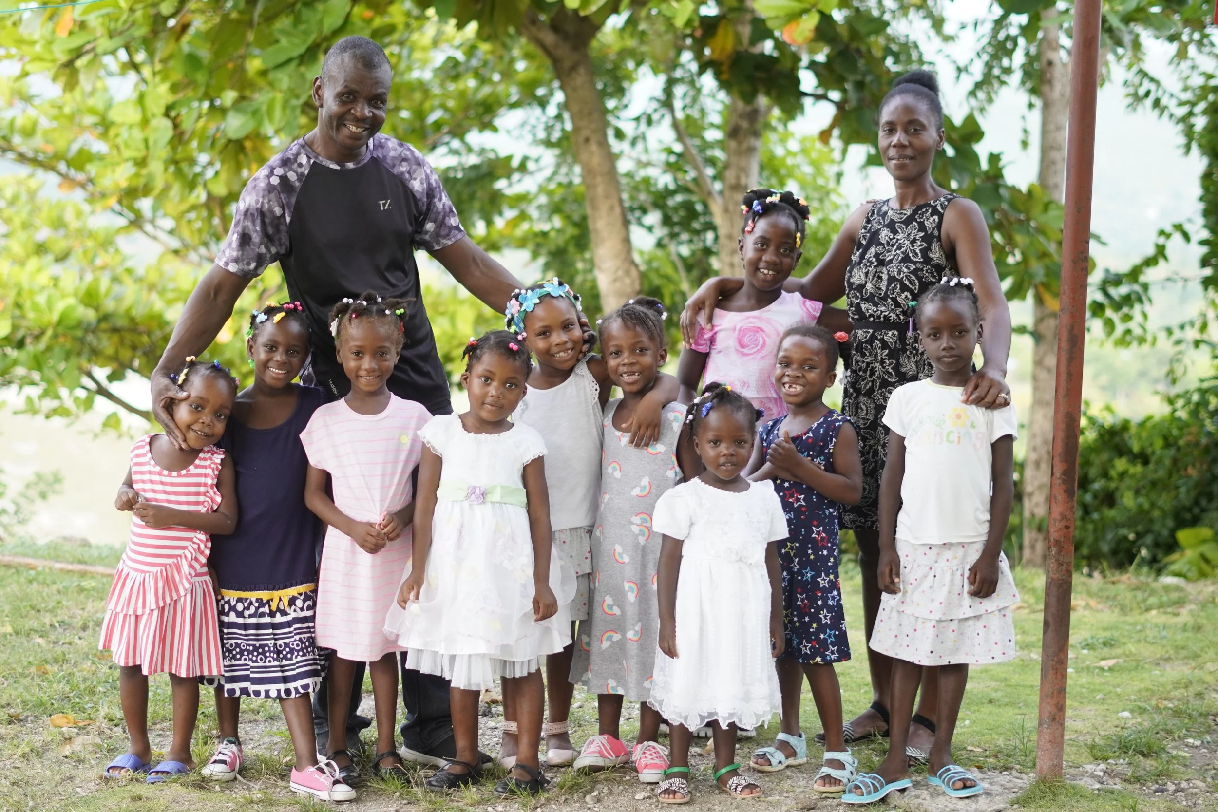 A Home of Hope family with a mom, dad, and twelve little girls all smile with arms around each other