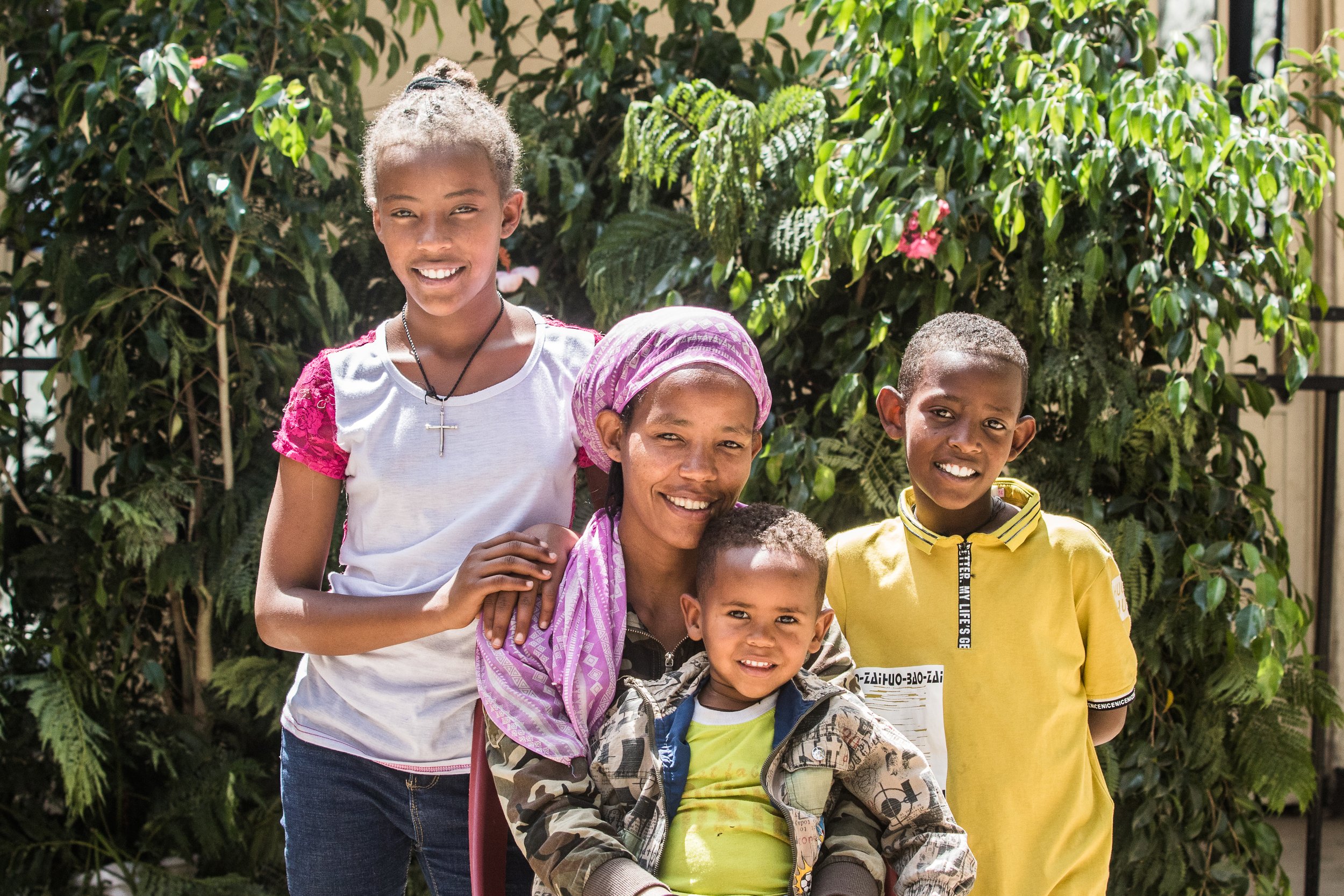 A young mother holding her little girl and smiling with her little son and older daughter