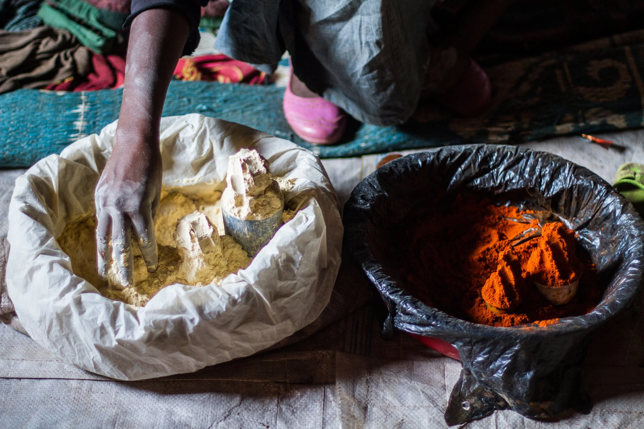 A woman measures from two large bowls of spices