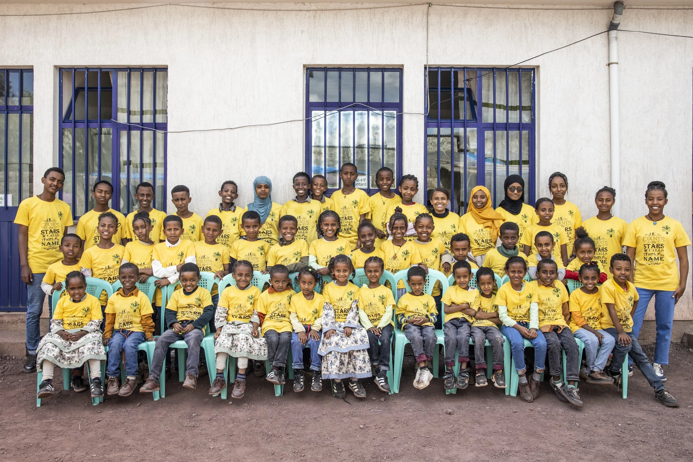 Large group of young Ethiopian children smiling and all wearing matching yellow shirts