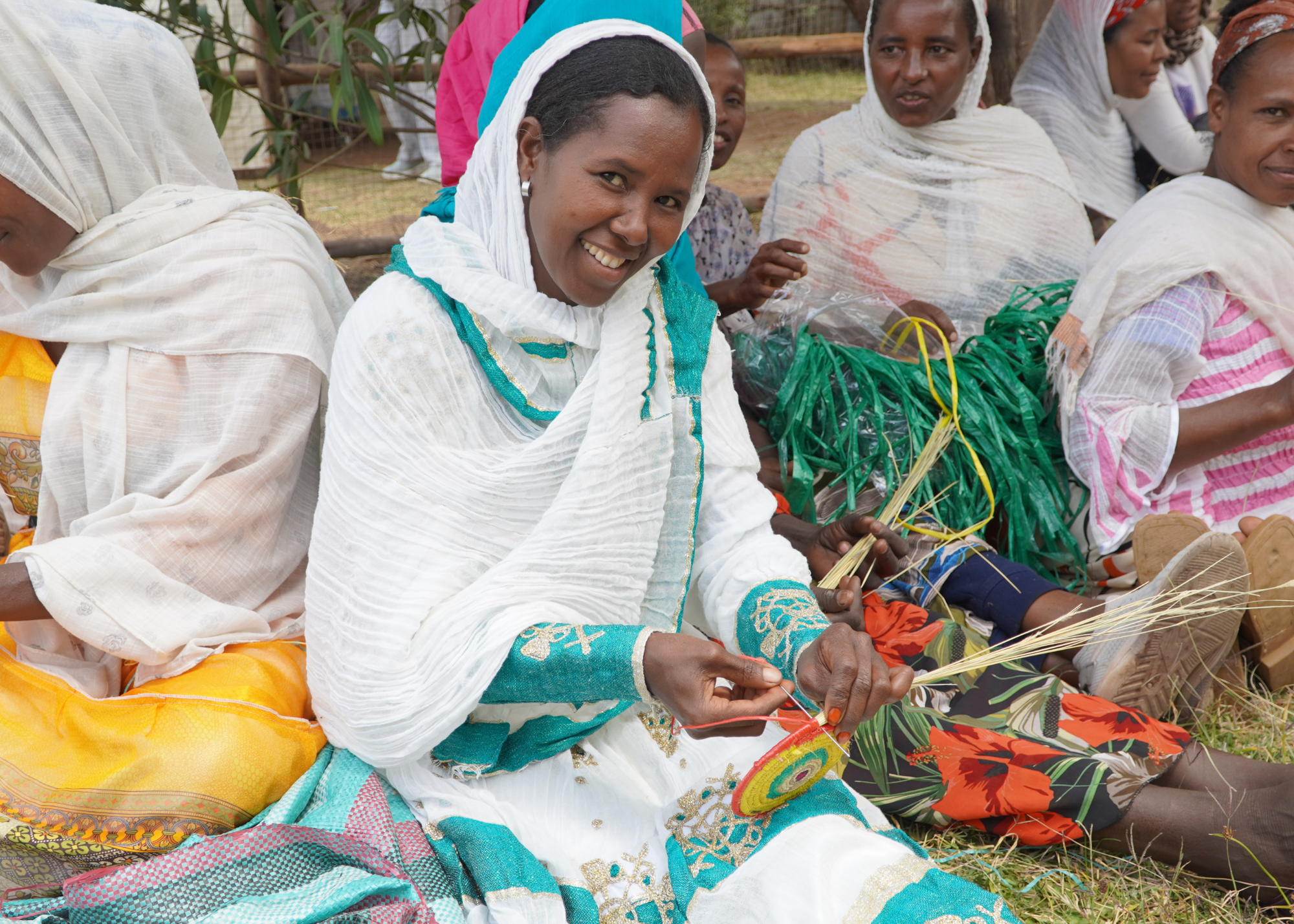 Young mother smiling as she weaves a colorful basket with straw