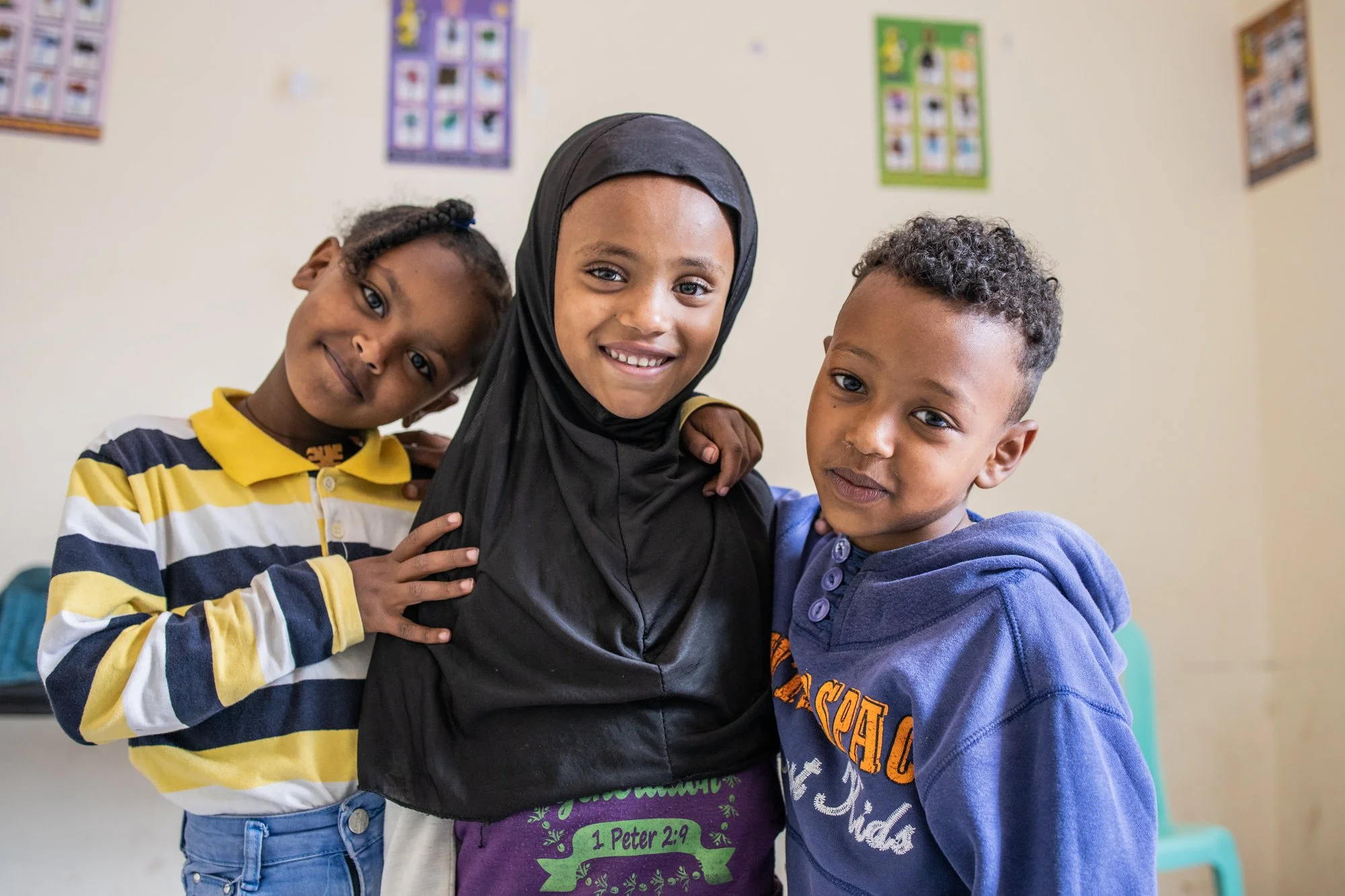 Three young friends smile with arms around each other