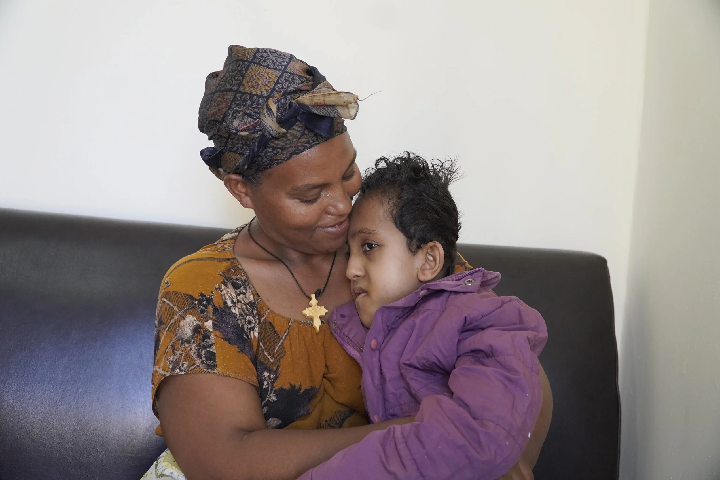 Young mother holds and smiles at her little boy with disabilities